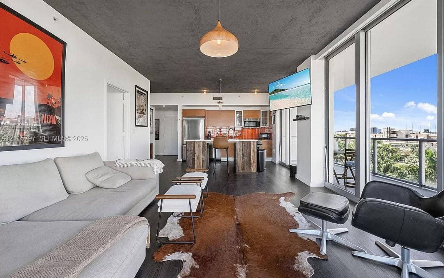 Open-concept area featuring floor-to-ceiling glass panels, wood-finish cabinetry, a central kitchen island with wood detailing, dark wood-finish flooring, and a textured charcoal-toned ceiling