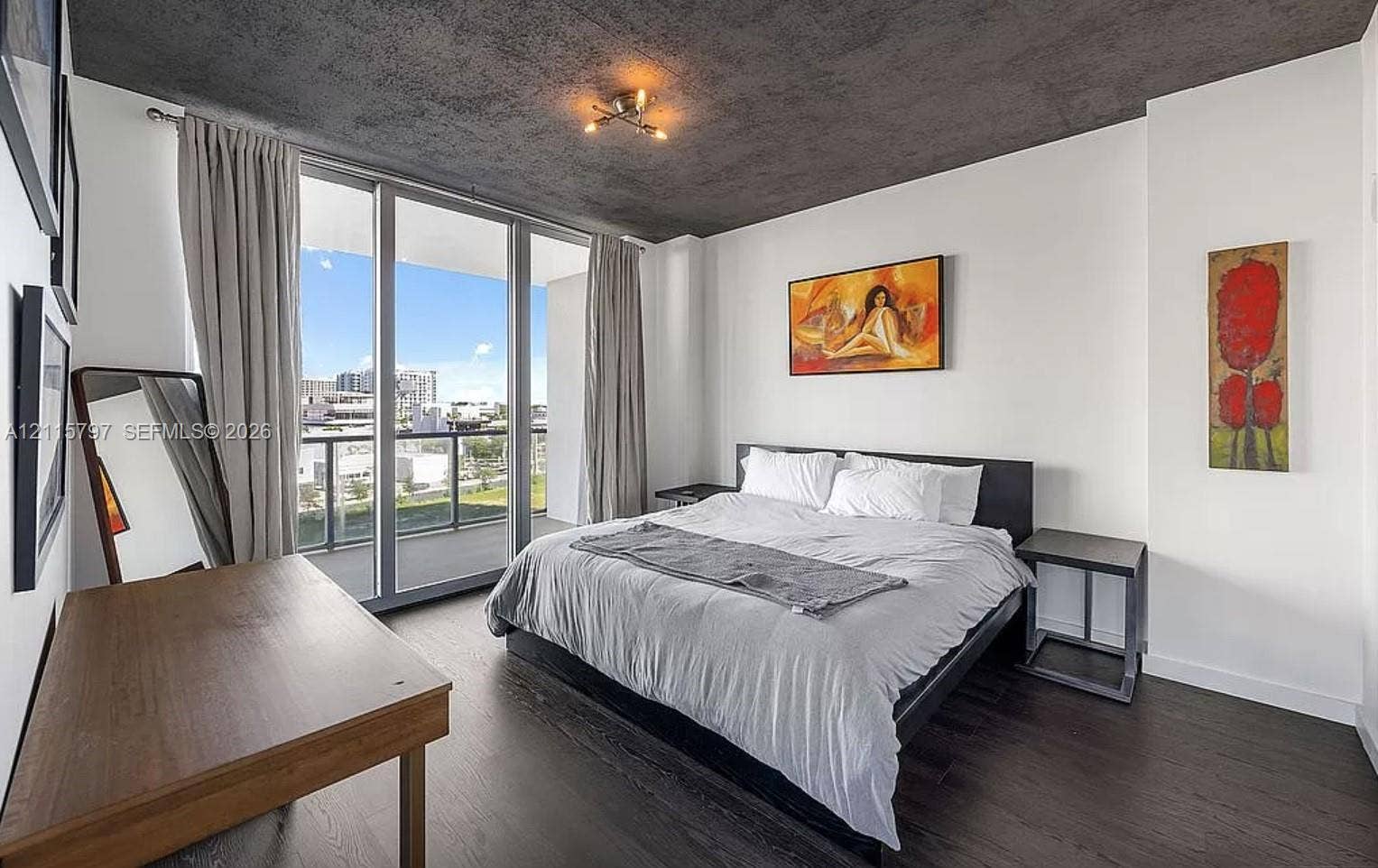 Floor-to-ceiling glass sliding doors opening to a balcony, dark wood-finish flooring, and a textured concrete-style ceiling