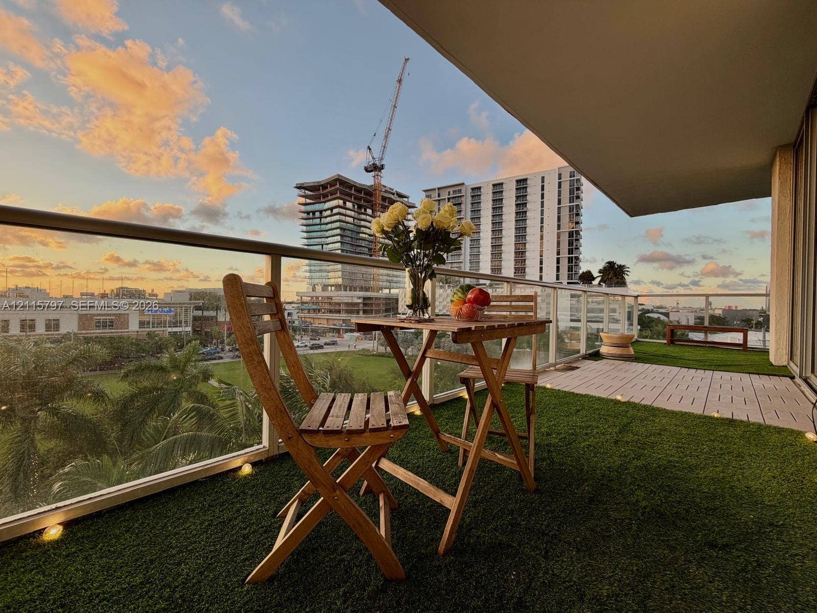 Covered balcony featuring synthetic grass flooring, integrated recessed lighting, and a glass-paneled railing