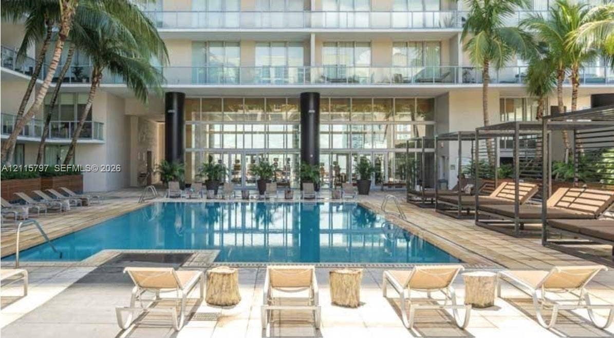 Swimming pool featuring stone tile decking, perimeter glass balcony railings, and covered cabana structures