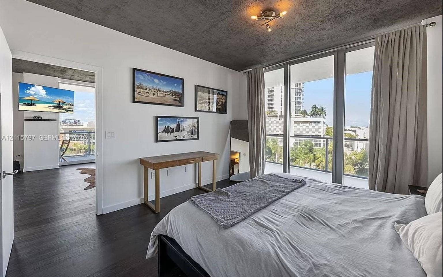 Interior space featuring exposed concrete ceiling, wood-finish flooring, and floor-to-ceiling windows with access to a private balcony