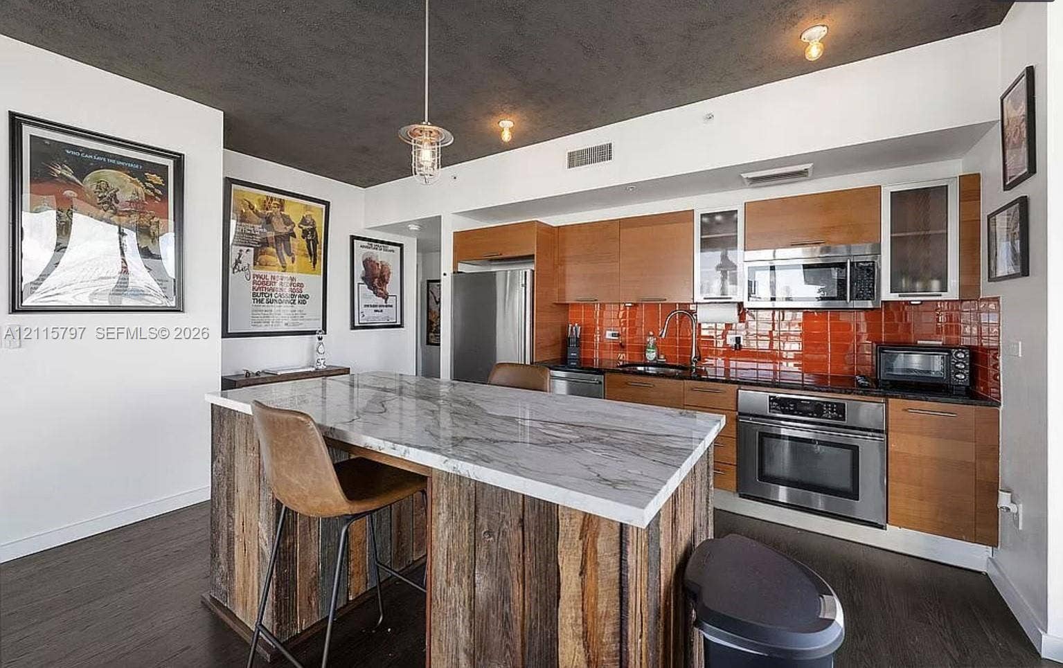 Kitchen featuring flat-panel wood cabinetry, stone-finish countertops, stainless steel appliances, a tile backsplash, and a rustic wood-clad island