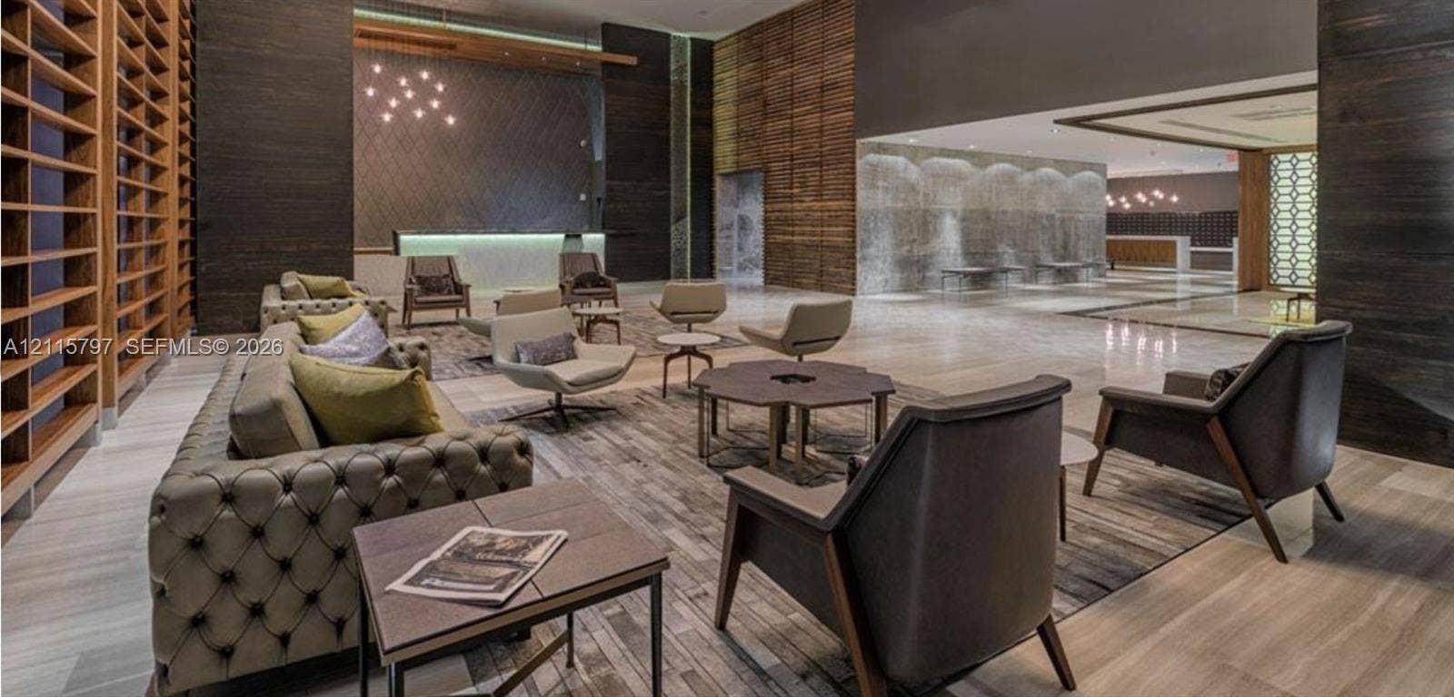 Double-height ceiling lobby featuring stone-surround wall paneling, built-in floor-to-ceiling wooden shelving, polished stone flooring, and a decorative interior water feature