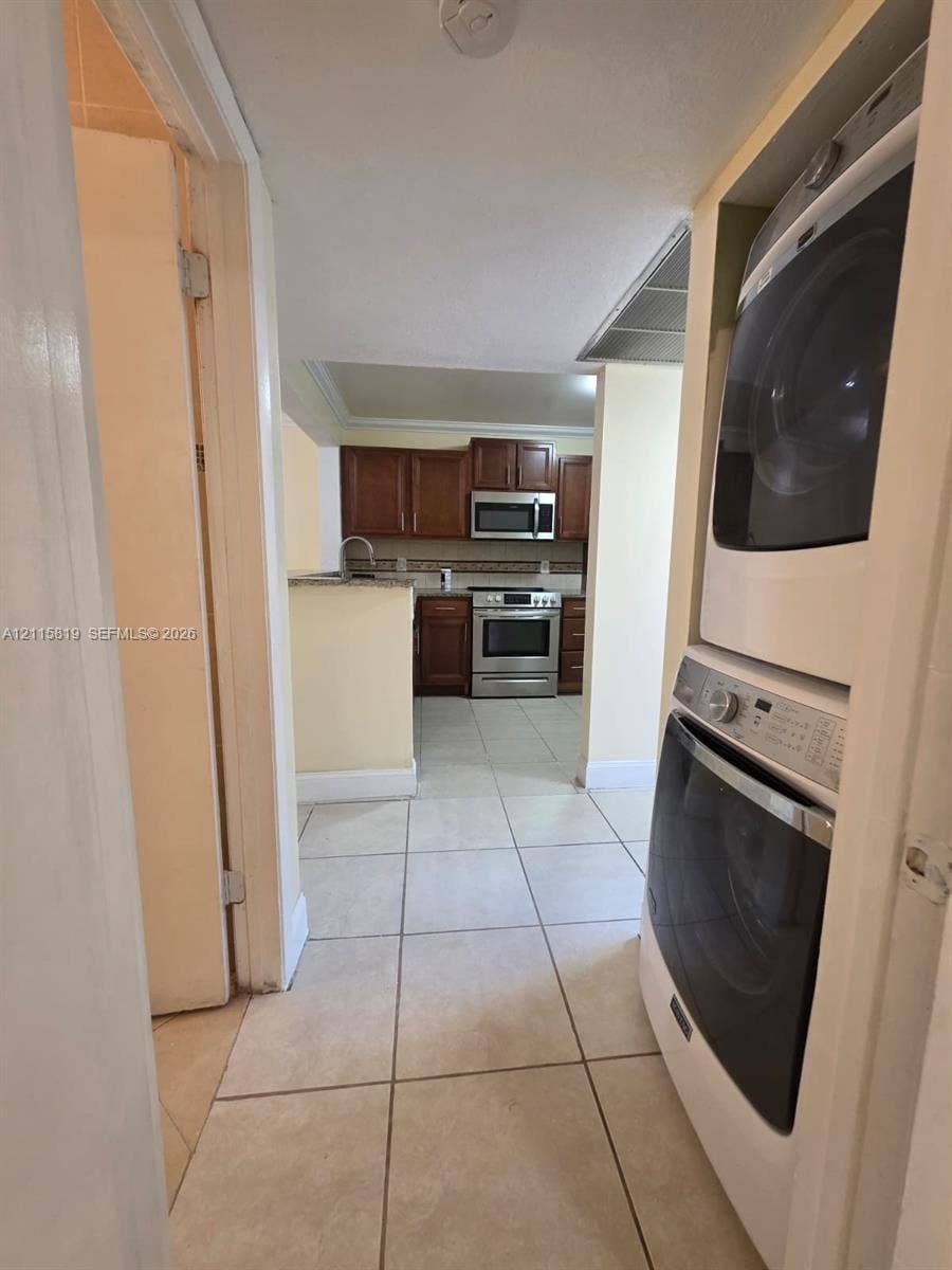 831 NE 207th Lane, #2-203, Miami, Miami, FL 33179 Laundry area featuring a stackable washer and dryer, tiled flooring, wood-toned cabinetry, stainless steel appliances, and stone-finish countertops