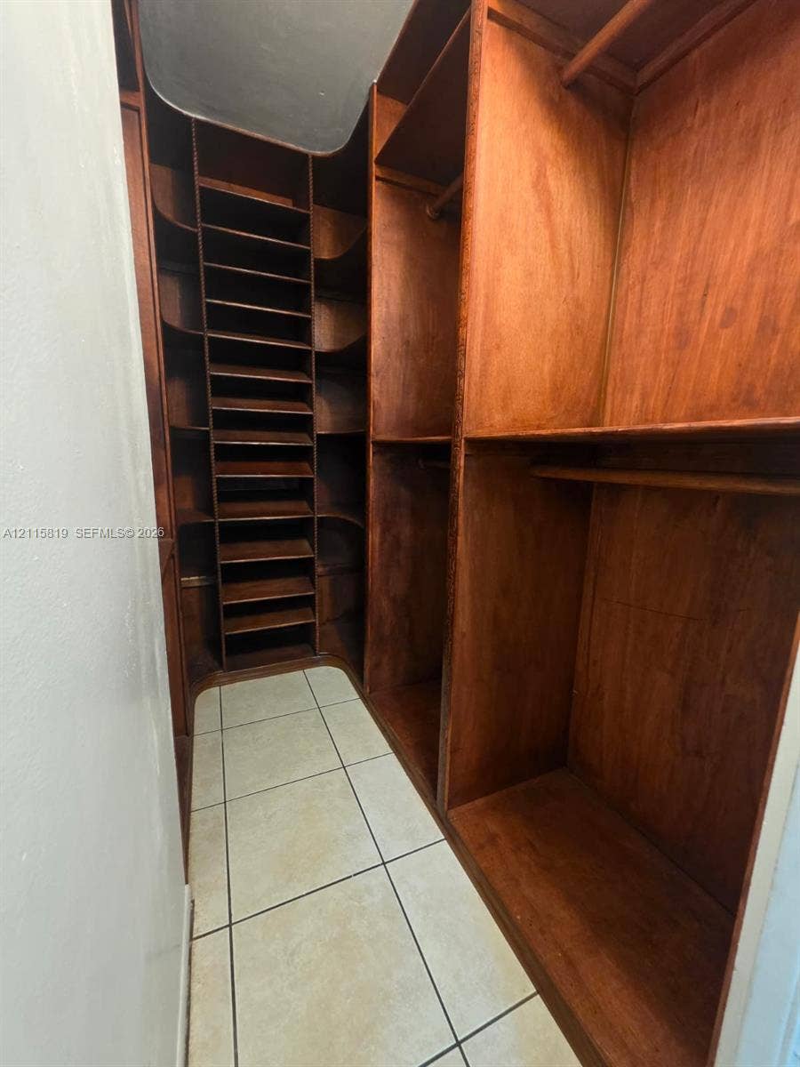 831 NE 207th Lane, #2-203, Miami, Miami, FL 33179 Custom wood-finish cabinetry featuring integrated shelving, vertical storage compartments, and hanging rods, complemented by tile flooring