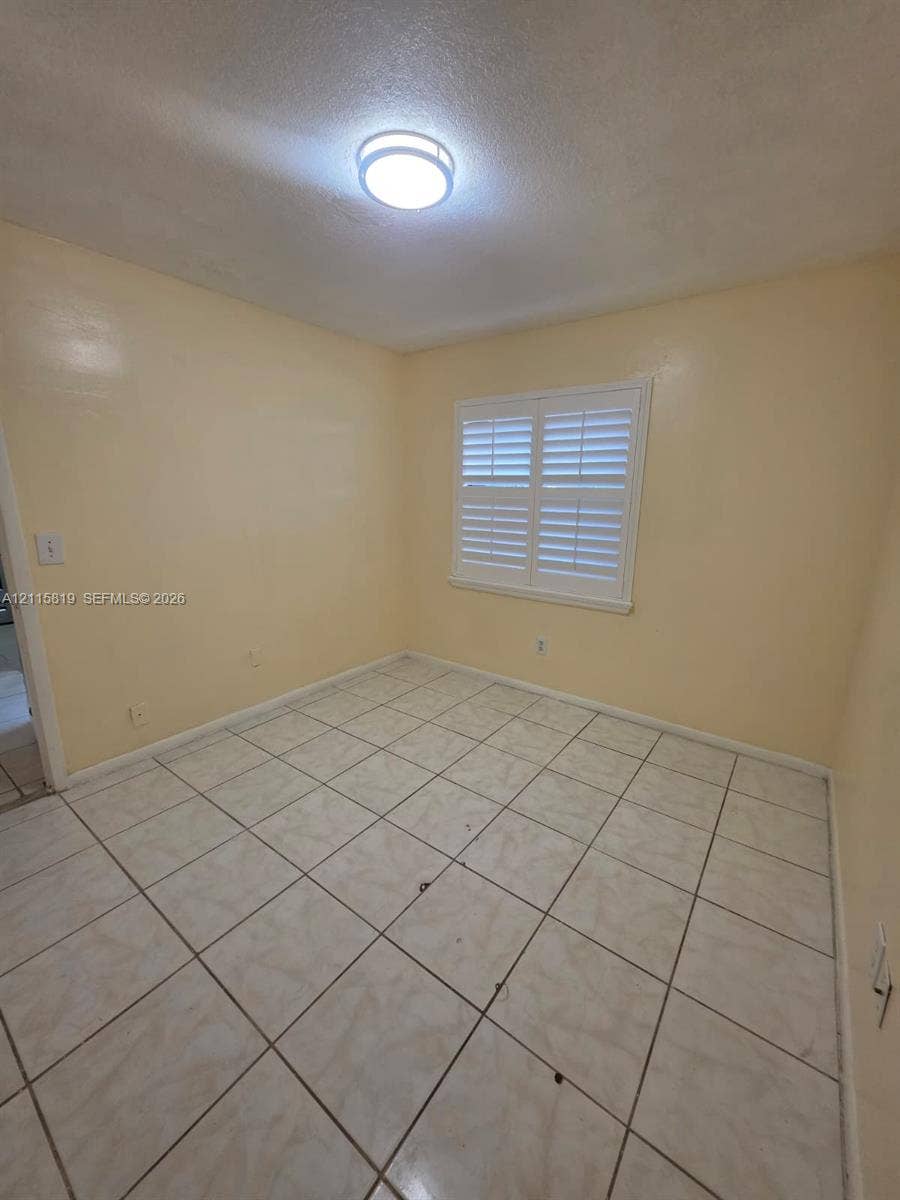 831 NE 207th Lane, #2-203, Miami, Miami, FL 33179 Interior room featuring large-format ceramic tile flooring, neutral wall tones, and white plantation shutters