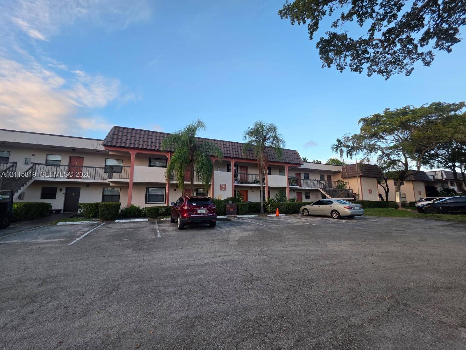 831 NE 207th Lane, #2-203, Miami, Miami, FL 33179 Multi-story exterior featuring a tile roof, paved surface parking, mature palm trees, and ground-level landscaping