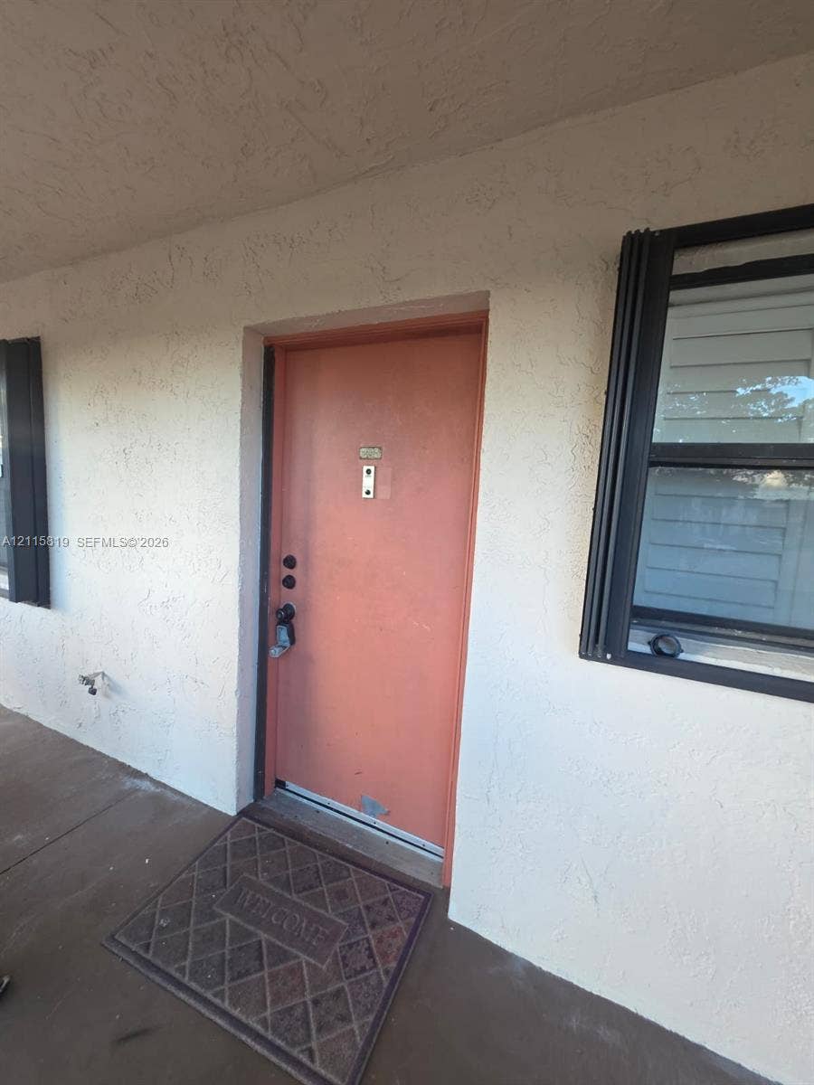 831 NE 207th Lane, #2-203, Miami, Miami, FL 33179 Exterior entry featuring a solid door, integrated door knocker, and metal-framed window with exterior casing