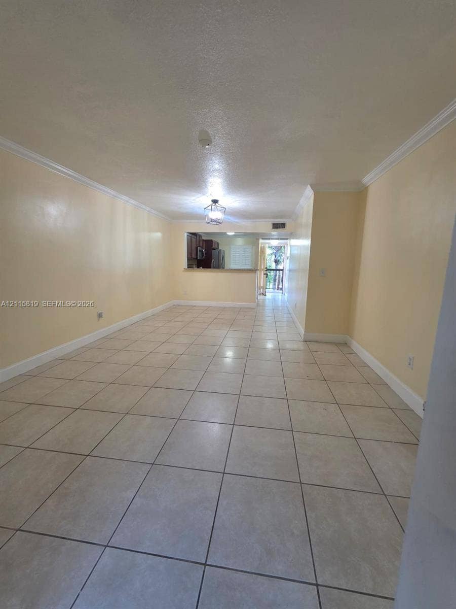 831 NE 207th Lane, #2-203, Miami, Miami, FL 33179 Open-concept area featuring light-toned tile flooring, crown molding, and a pass-through opening into the kitchen area with a ceiling-mounted lantern light fixture