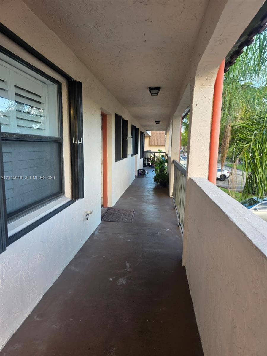 831 NE 207th Lane, #2-203, Miami, Miami, FL 33179 Covered exterior walkway featuring stucco walls, flush-mount lighting, dark-toned concrete flooring, and metal railings