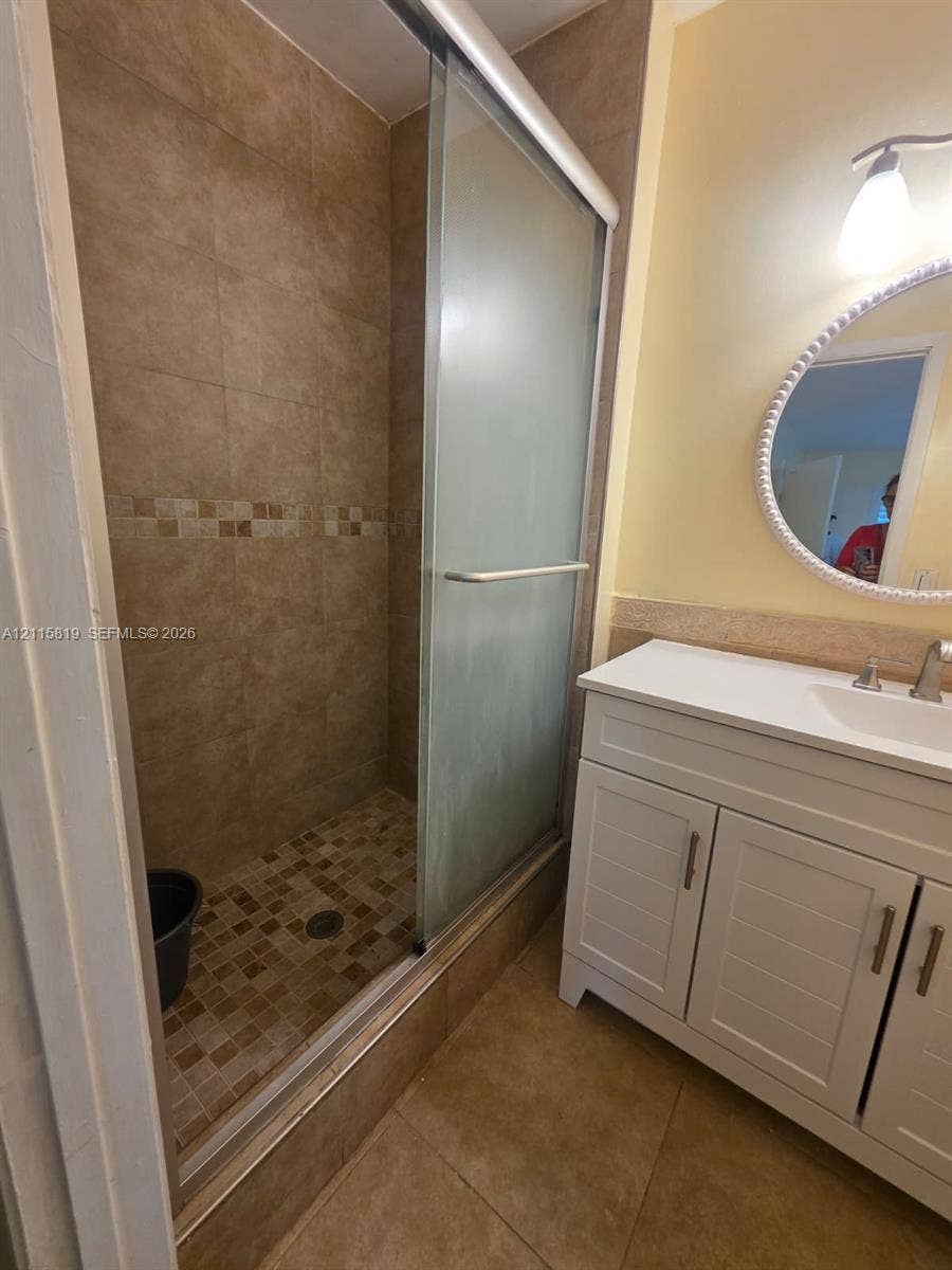 831 NE 207th Lane, #2-203, Miami, Miami, FL 33179 Bathroom featuring a walk-in shower with a glass sliding door, mosaic tile flooring, neutral wall tiling, white cabinetry, and a countertop-integrated sink