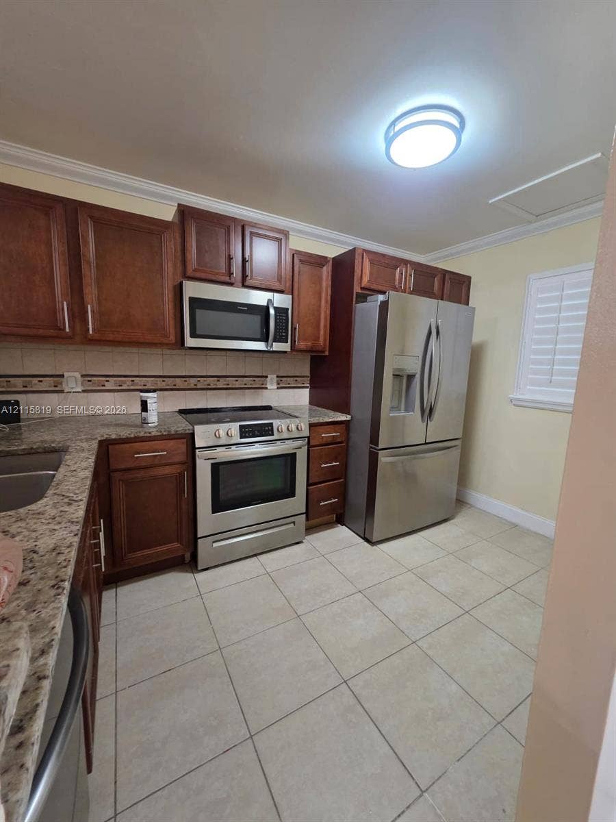 831 NE 207th Lane, #2-203, Miami, Miami, FL 33179 Kitchen featuring stained wood cabinetry, stone-surface countertops, stainless steel appliances, and ceramic tile flooring