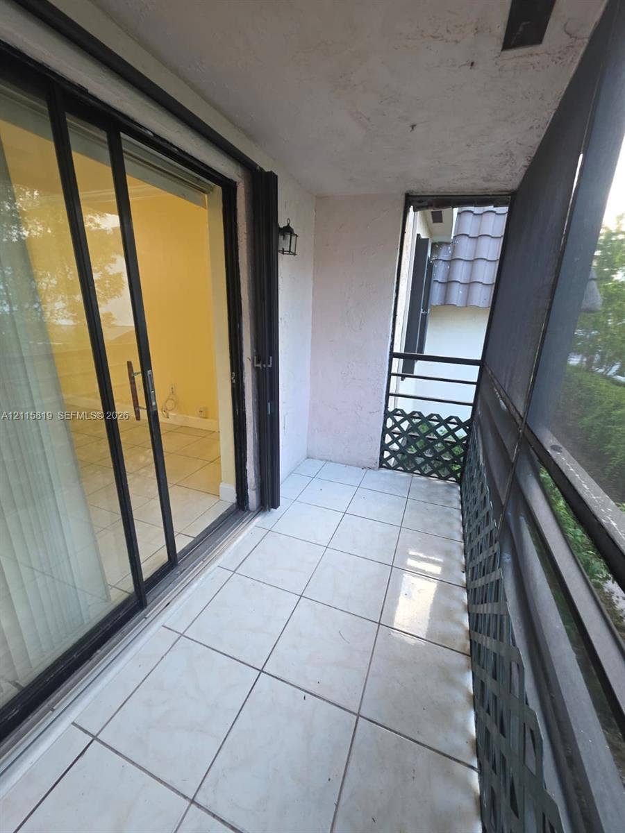 831 NE 207th Lane, #2-203, Miami, Miami, FL 33179 Covered balcony featuring square tile flooring, black metal railing with lattice detailing, and sliding glass door access