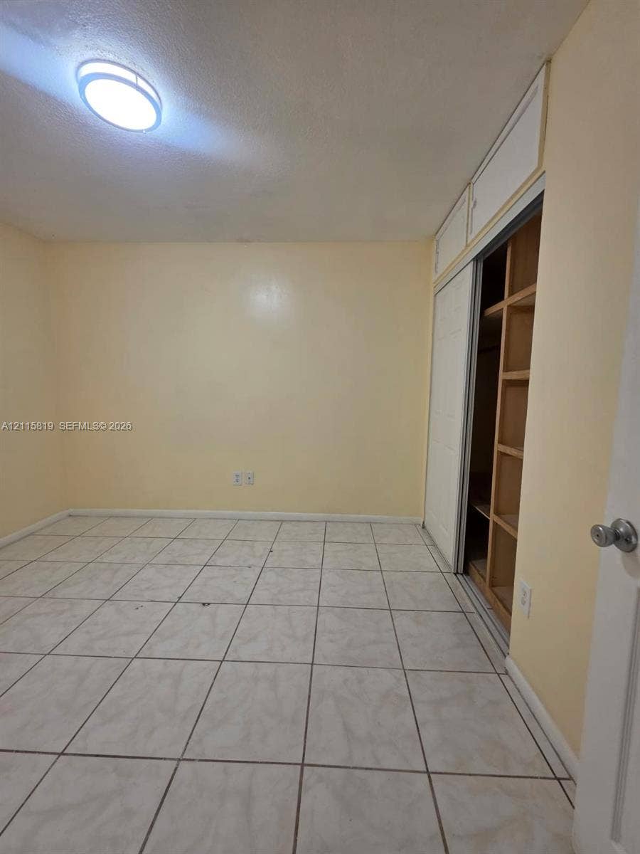 831 NE 207th Lane, #2-203, Miami, Miami, FL 33179 Ceramic tile flooring, flush-mount ceiling light fixture, and closet with sliding doors and integrated shelving
