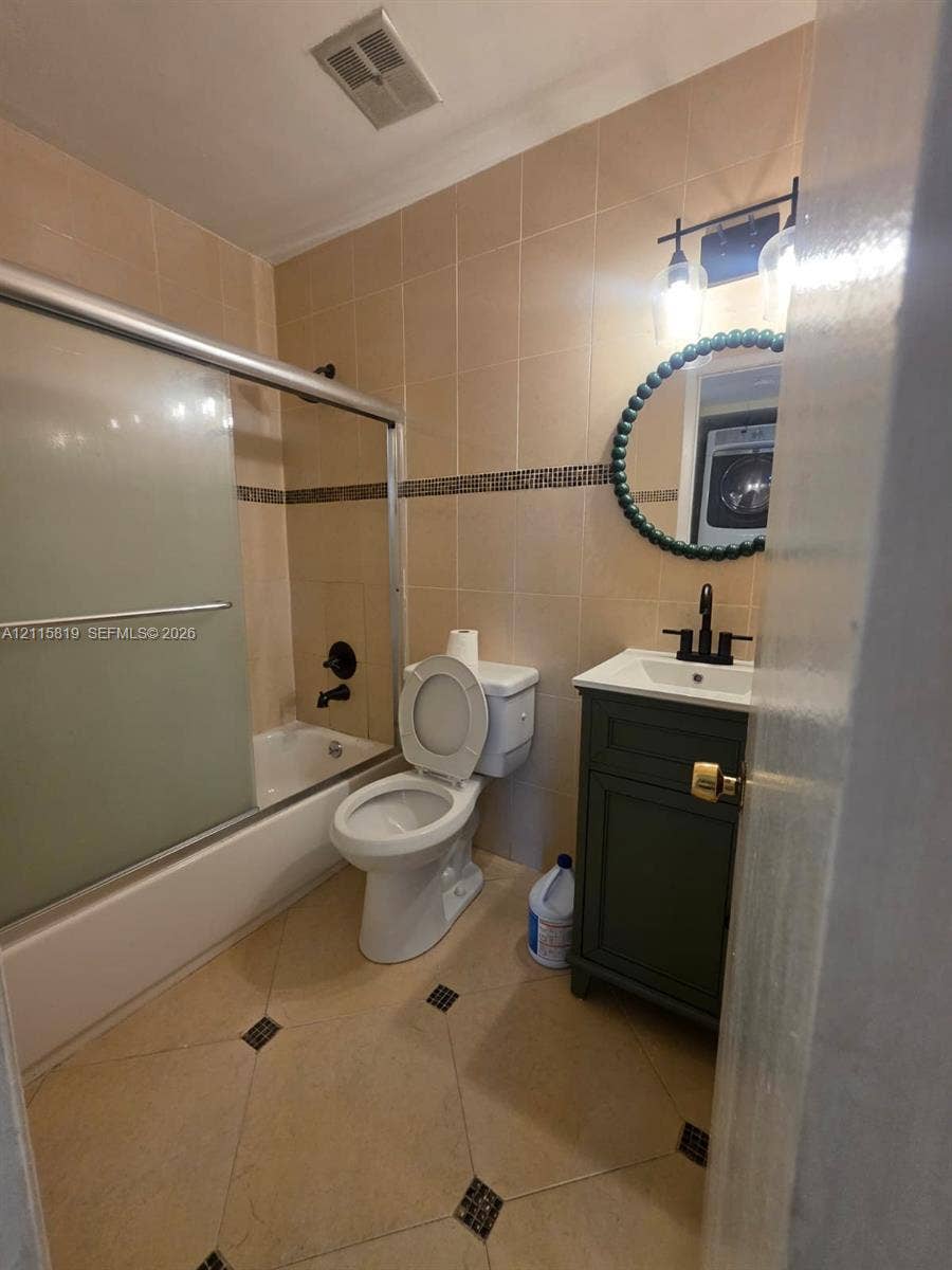 831 NE 207th Lane, #2-203, Miami, Miami, FL 33179 Bathroom featuring a vanity with a white countertop and dark cabinetry, a soaking tub with a sliding glass door, a matte black faucet, and stone-finish floor tiling with decorative inserts