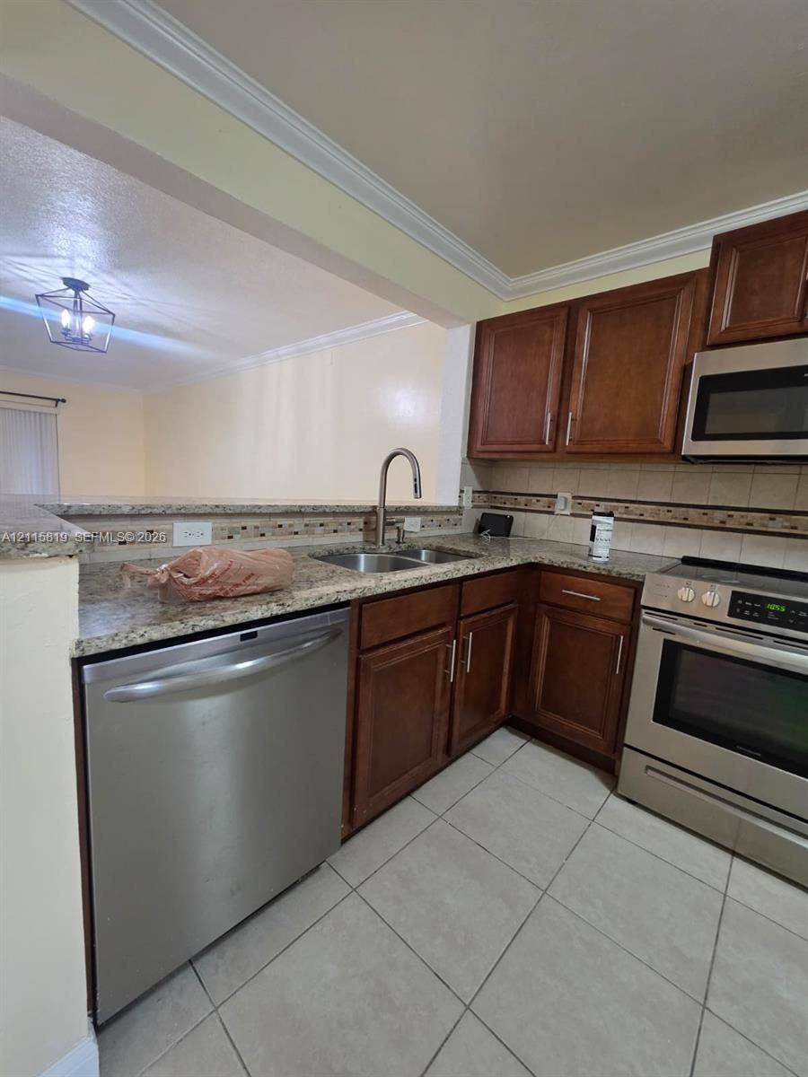 831 NE 207th Lane, #2-203, Miami, Miami, FL 33179 Kitchen featuring medium-toned wood cabinetry, stone-patterned countertops, stainless steel appliances, ceramic tile flooring, and crown molding