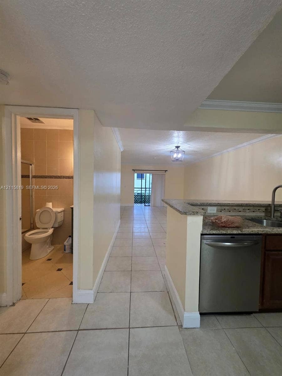 831 NE 207th Lane, #2-203, Miami, Miami, FL 33179 Kitchen featuring stone-finish countertops, stainless steel dishwasher, and dark wood-finish cabinetry, complemented by uniform tile flooring and crown molding throughout the interior