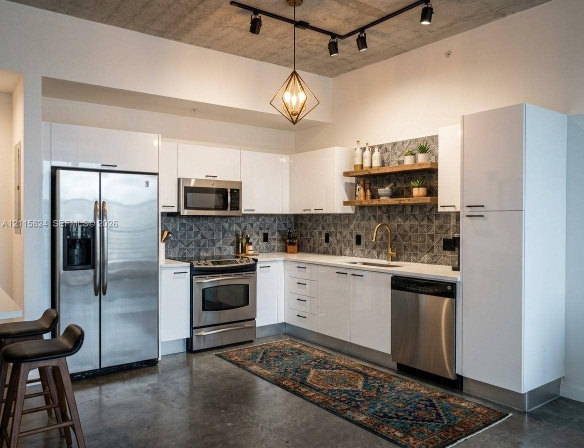 133 2 Avenue, #2908, Miami, Miami, FL 33132 Modern kitchen featuring sleek white cabinetry, stainless steel appliances, patterned tile backsplash, floating wood shelving, and exposed concrete ceiling