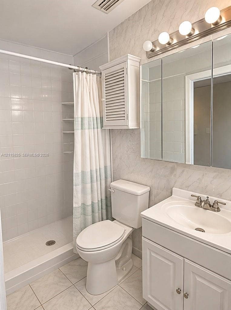 7130 W 12th Court, Hialeah, FL 33014 Bathroom featuring a tiled walk-in shower with integrated shelving, white vanity with an integrated sink, three-panel medicine cabinet, and wall-mounted light fixture