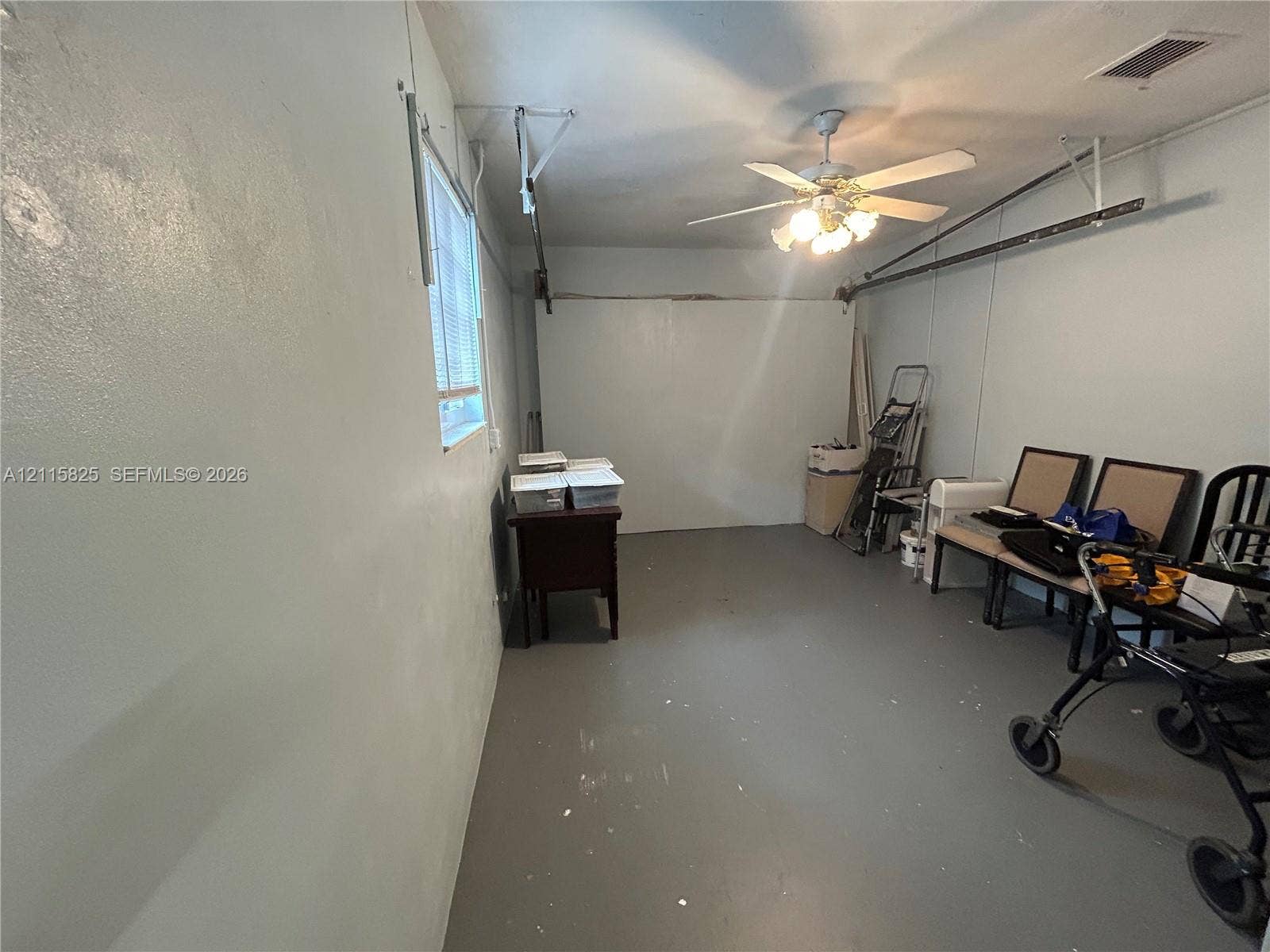 7130 W 12th Court, Hialeah, FL 33014 Enclosed garage featuring painted concrete flooring, a single window, and a ceiling-mounted light fixture with a fan