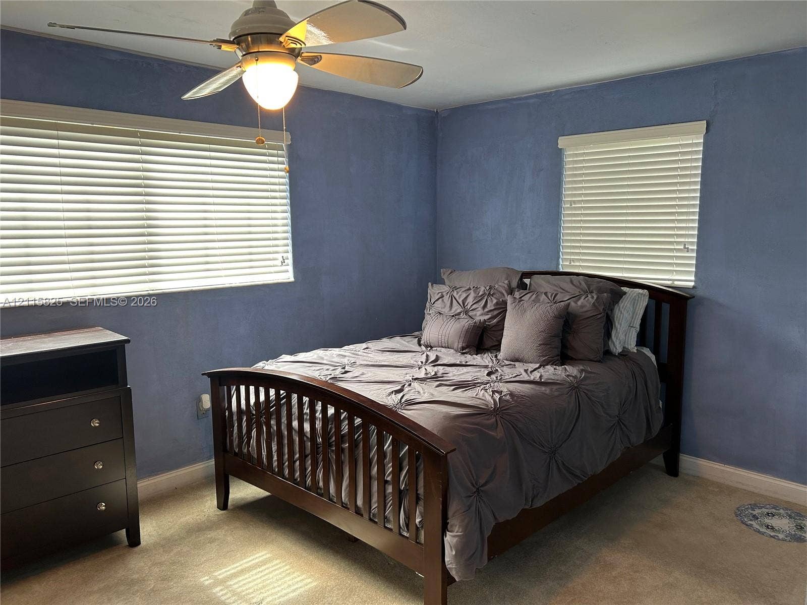 7130 W 12th Court, Hialeah, FL 33014 Neutral-toned carpeting, dual windows with horizontal blinds, and a multi-blade ceiling fan with an integrated light fixture