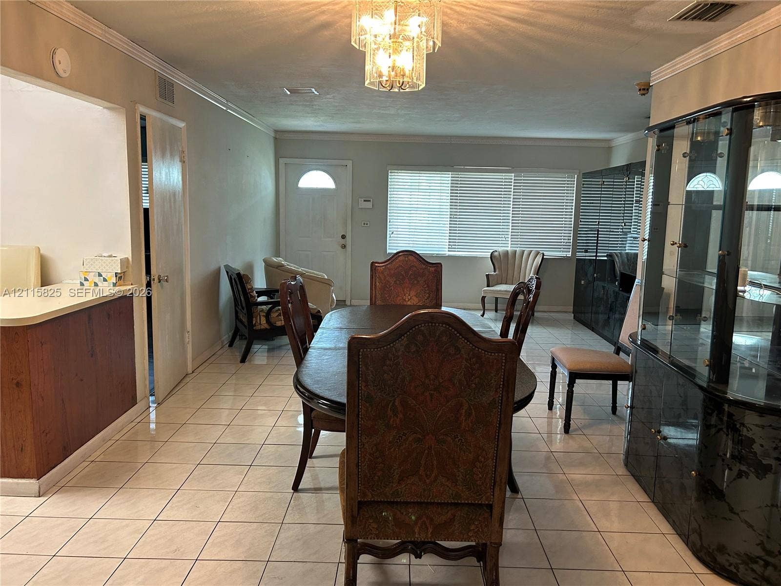 7130 W 12th Court, Hialeah, FL 33014 Open-concept interior featuring light-toned tile flooring, recessed crown molding, and a multi-tiered crystal chandelier