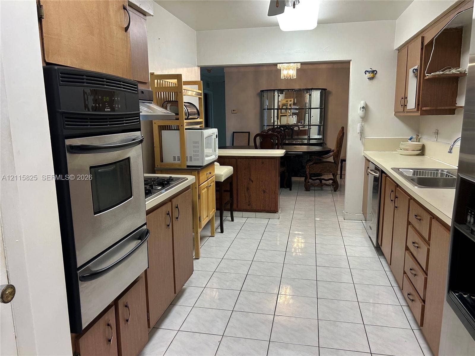 7130 W 12th Court, Hialeah, FL 33014 Kitchen featuring wood cabinetry, stainless steel wall-mounted oven, solid surface countertops, a stainless steel dual-basin sink, and tile flooring