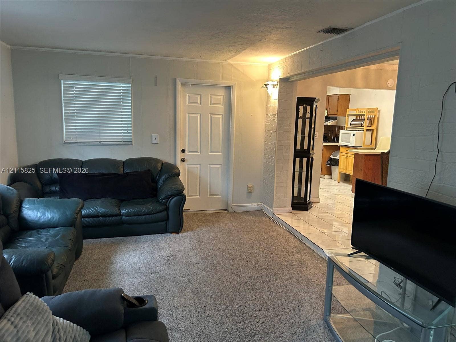 7130 W 12th Court, Hialeah, FL 33014 Neutral interior space featuring wall-to-wall carpeting, white textured masonry wall accents, six-panel entry door, and tiled flooring surface in the secondary area