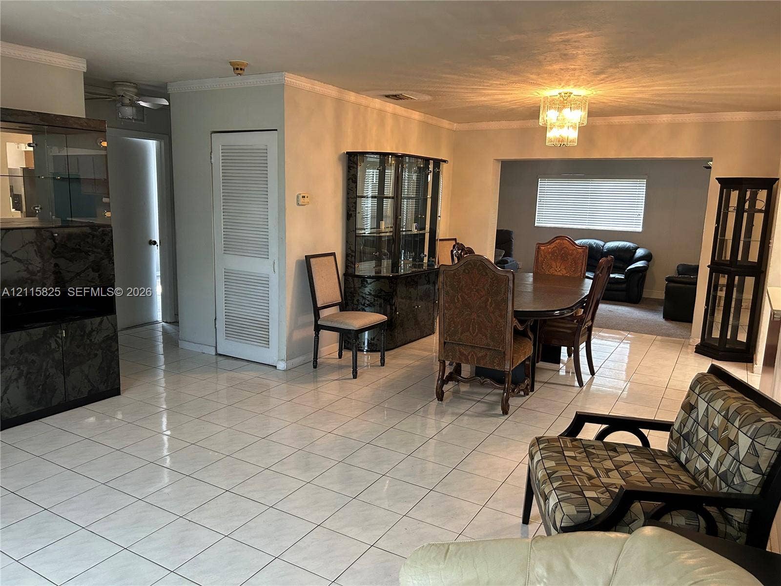 7130 W 12th Court, Hialeah, FL 33014 Open-concept interior featuring light-toned tile flooring, crown molding, and a multi-tiered crystal chandelier