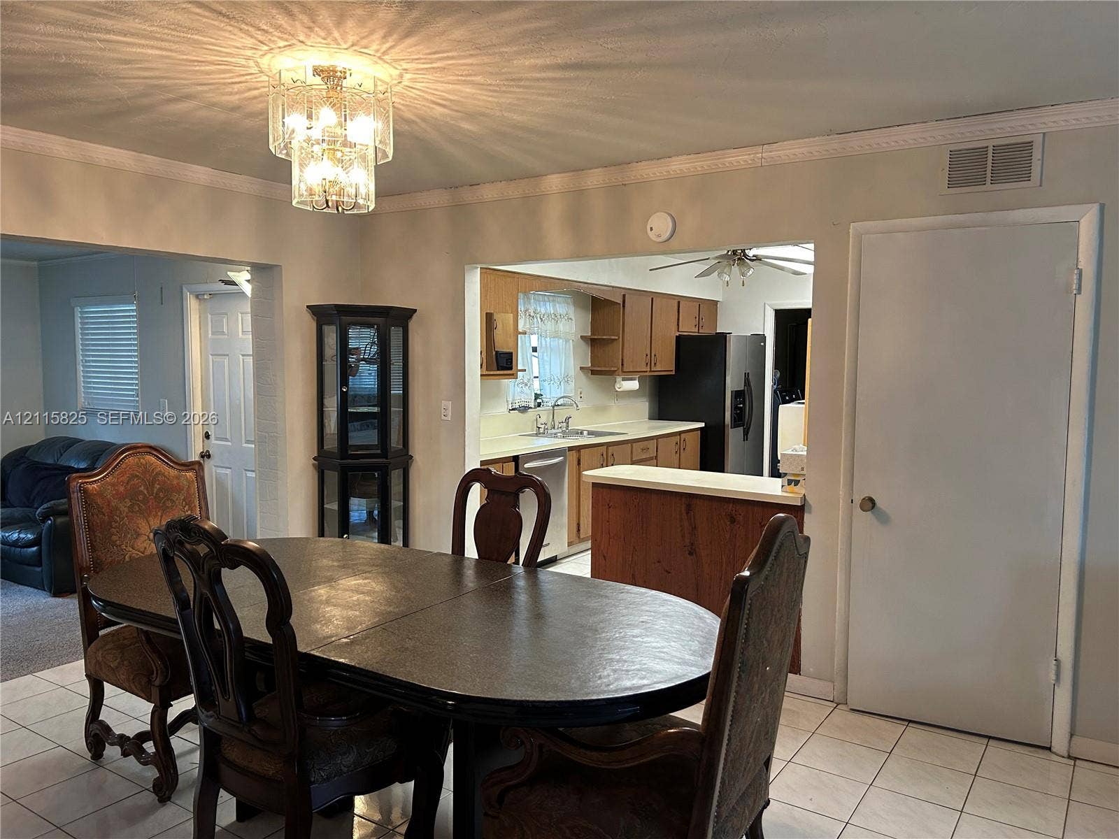 7130 W 12th Court, Hialeah, FL 33014 Dining area featuring a tiered crystal chandelier, tile flooring, and crown molding, with pass-through access to kitchen cabinetry and a built-in counter