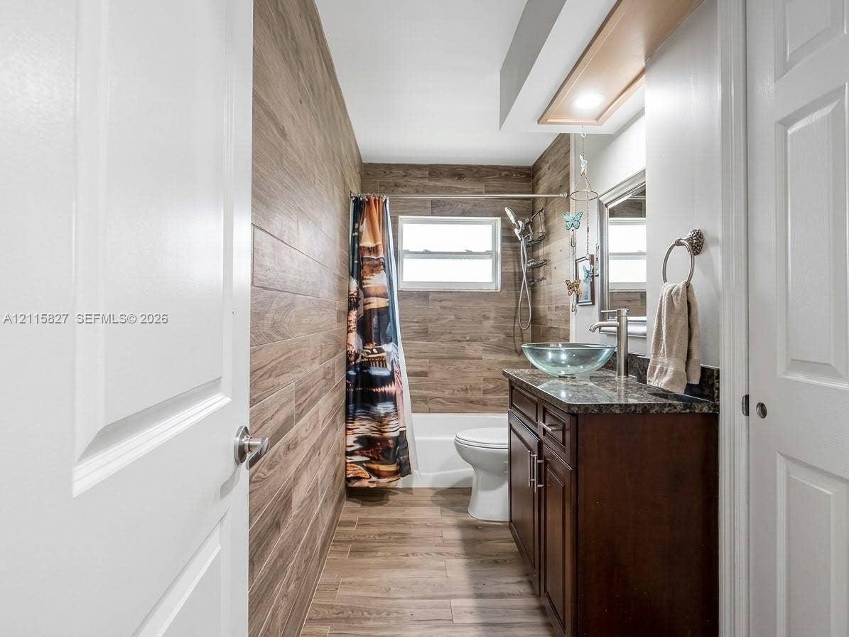 411 Wilma Circle, #0, Riviera Beach, Riviera Beach, FL 33404 Bathroom featuring wood-finish wall and floor tile, dark wood cabinetry, a stone-surface countertop, and a glass vessel sink