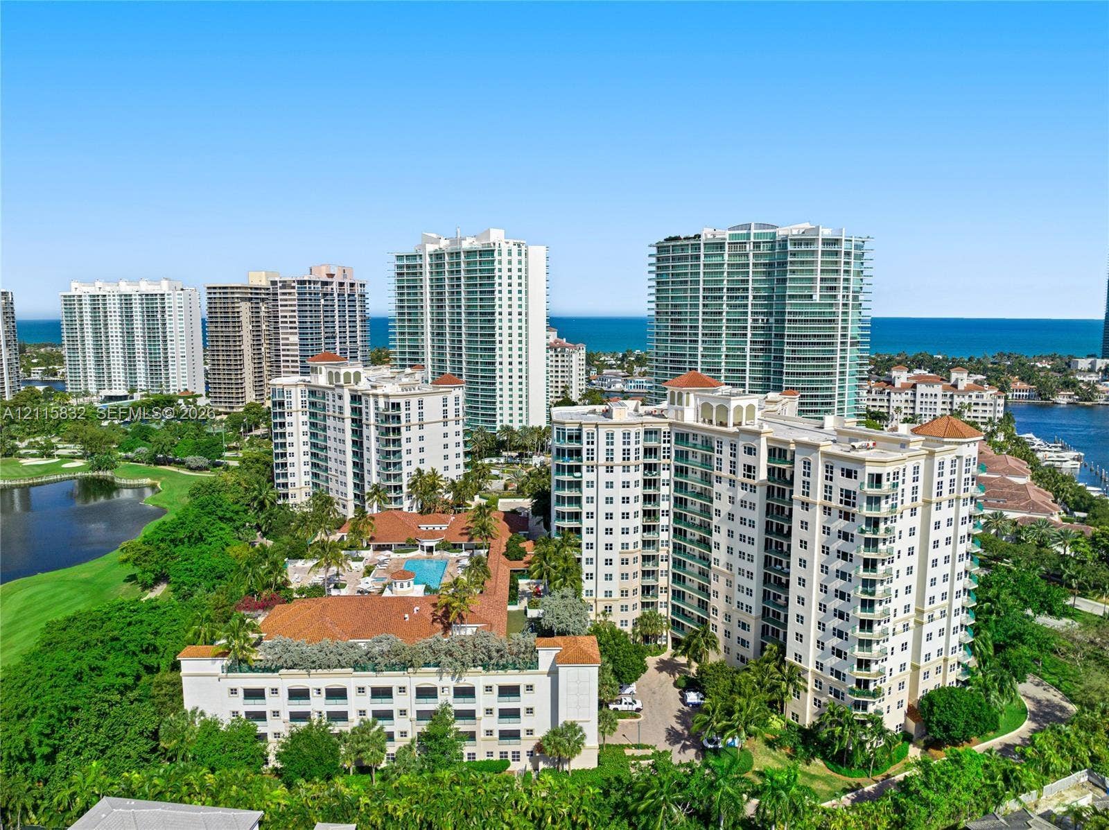 19900 E Country Club Drive, #607, Aventura, Aventura, FL 33180 High-rise residential exterior featuring terracotta tile roofing, multi-story balconies, outdoor swimming pool, and manicured grounds, set against a coastal skyline