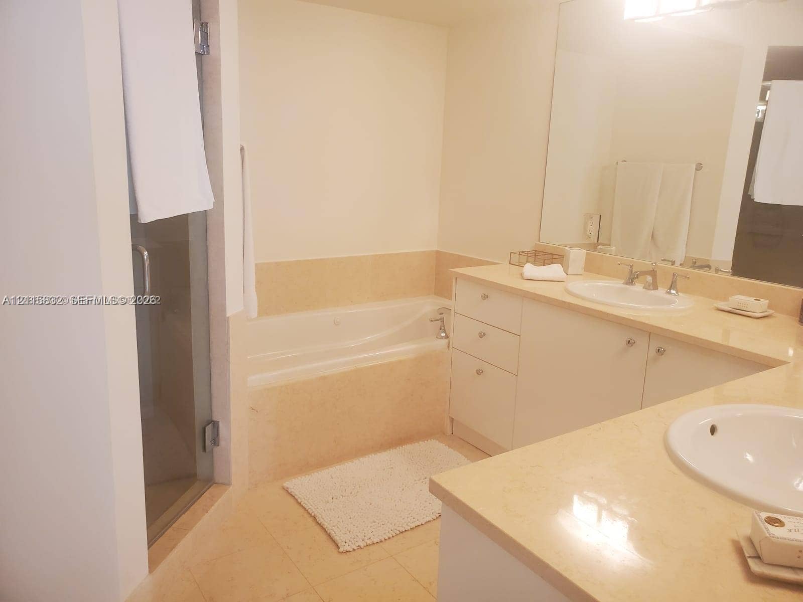 19900 E Country Club Drive, #607, Aventura, Aventura, FL 33180 Dual-vanity cabinetry with stone countertops, integrated oval sinks, a large wall-mounted mirror, and a recessed soaking tub with a glass-enclosed shower