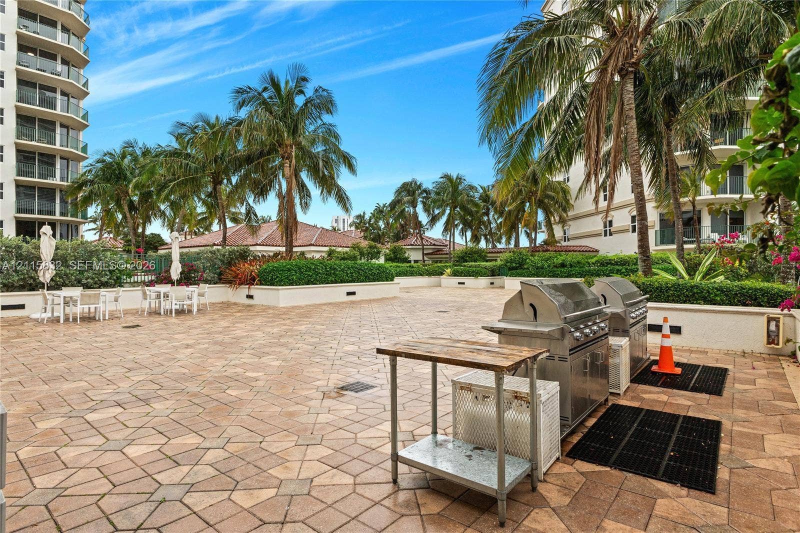 19900 E Country Club Drive, #607, Aventura, Aventura, FL 33180 Outdoor terrace featuring stone paver flooring, built-in stainless steel grilling stations, and mature palm tree landscaping