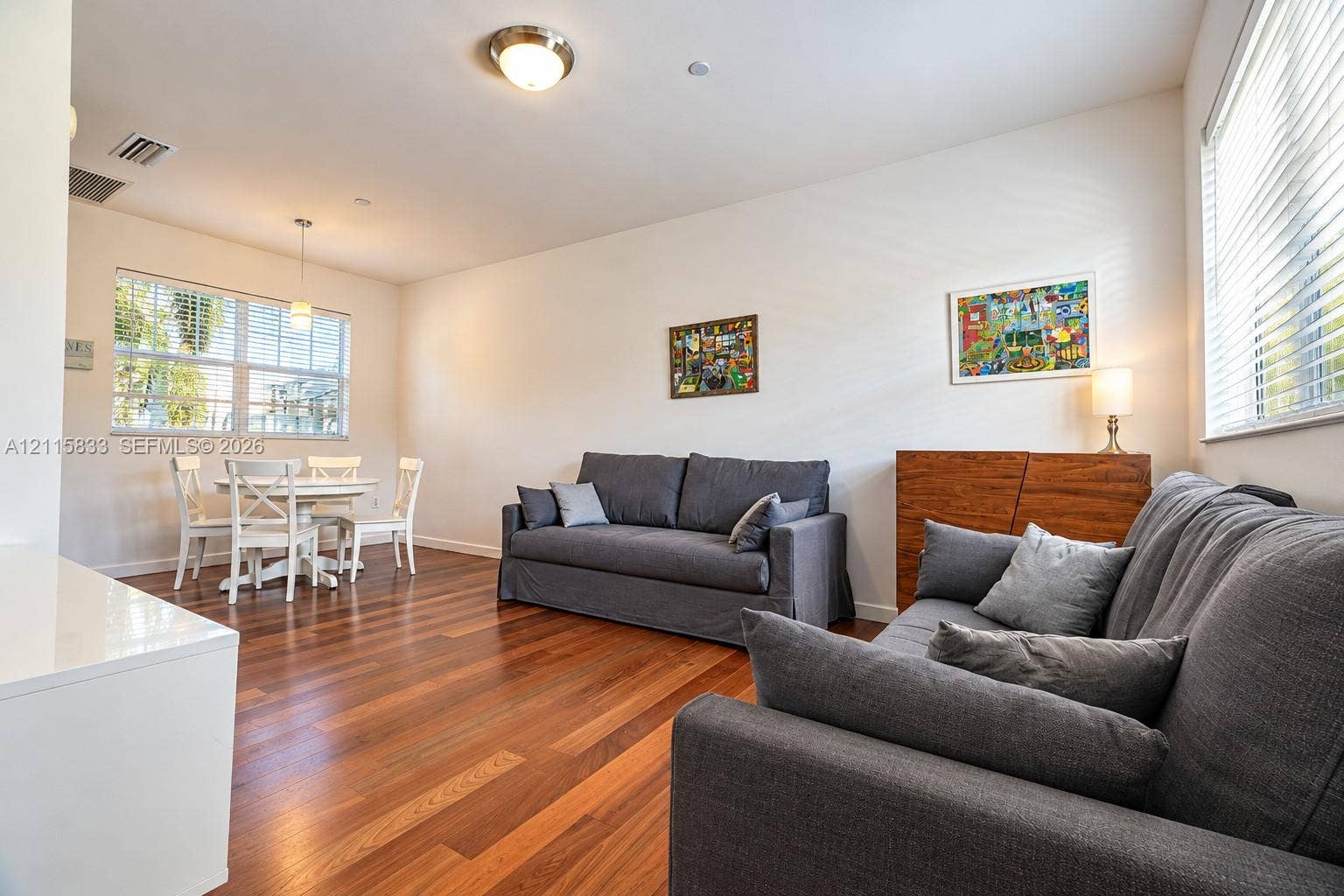 929 Meridian Avenue, #5, Miami Beach, FL 33139 Open interior space featuring wood-finish flooring, dual windows with horizontal blinds, a suspended pendant light fixture, and a central flush-mount ceiling light