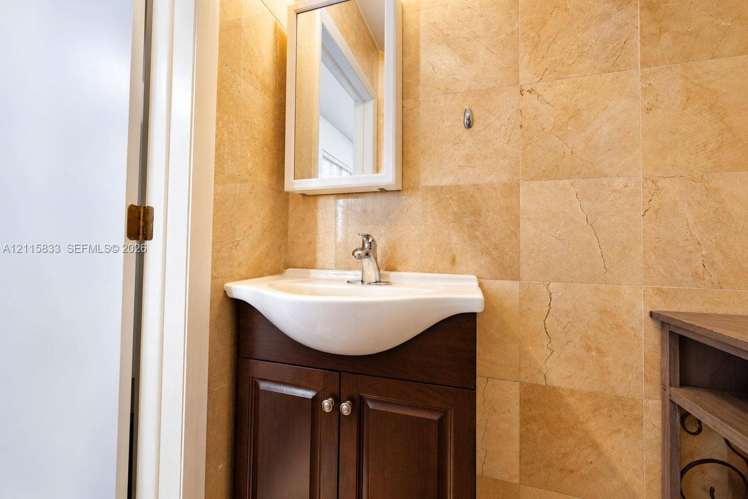 929 Meridian Avenue, #5, Miami Beach, FL 33139 Wall-mounted medicine cabinet with a mirrored door, white pedestal-style sink basin, dark wood-finish cabinet, and full-height stone-finish wall tiling