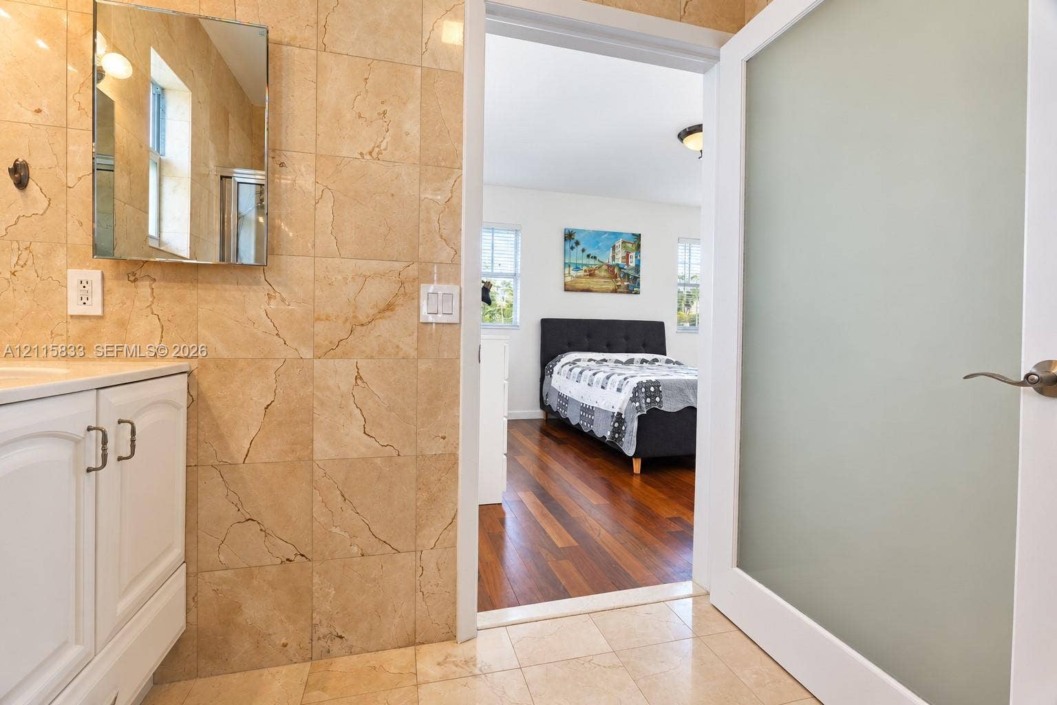 929 Meridian Avenue, #5, Miami Beach, FL 33139 Bathroom featuring large-format natural stone wall tiling, a white vanity with built-in cabinetry, and a frosted glass panel door with satin nickel hardware, opening to a space with wood-finish flooring