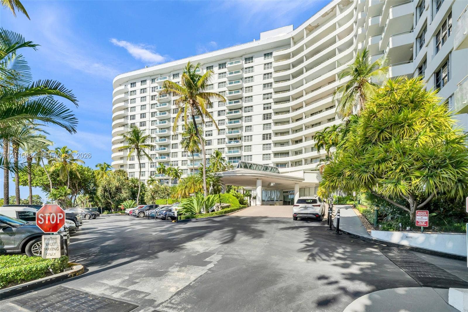 5161 Collins Avenue, #1717, Miami Beach, Miami Beach, FL 33140 Mid-rise exterior featuring curved structural architecture, stacked private balconies, a covered porte-cochre entry, and mature perimeter landscaping