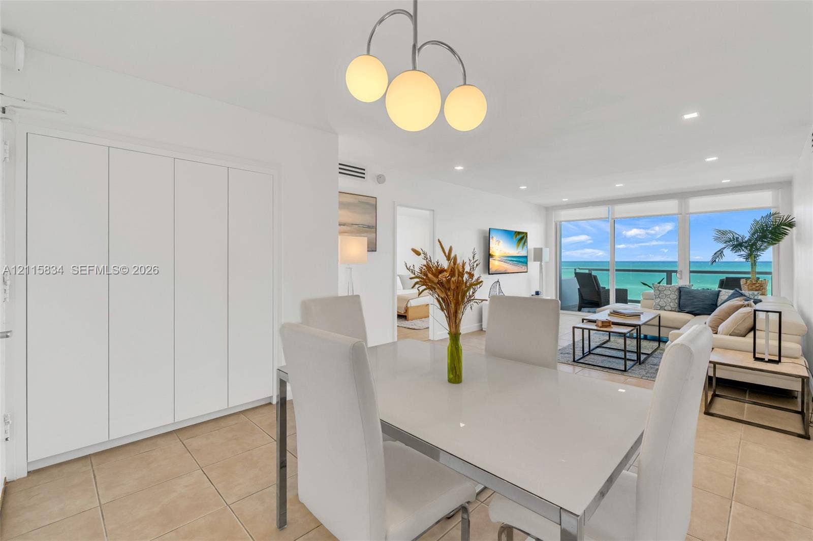 5161 Collins Avenue, #1717, Miami Beach, Miami Beach, FL 33140 Open-plan living area featuring large-format tile flooring, built-in floor-to-ceiling cabinetry, recessed lighting, a modern three-globe pendant fixture, and glass sliding doors providing water access