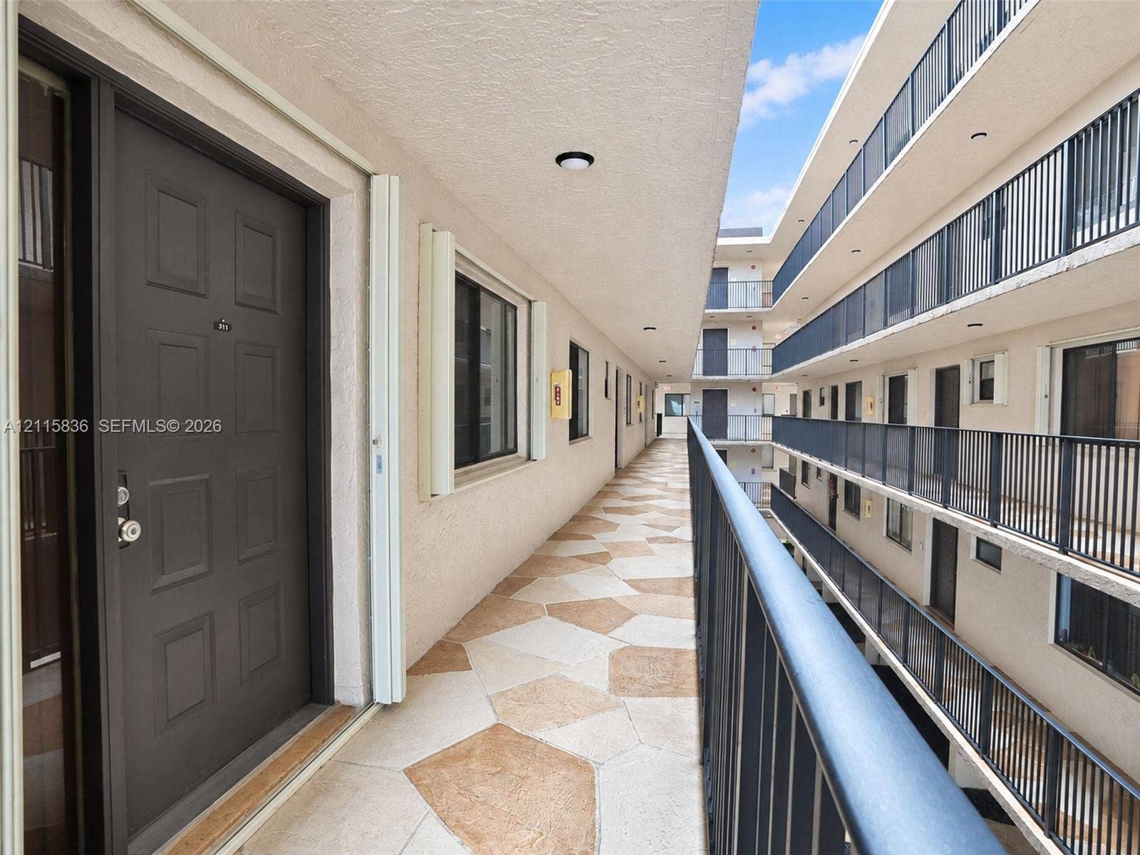 8000 Hampton Boulevard, #311, North Lauderdale, North Lauderdale, FL 33068 Exterior corridor featuring textured stone-pattern flooring, multi-story metal railings, and recessed ceiling lighting
