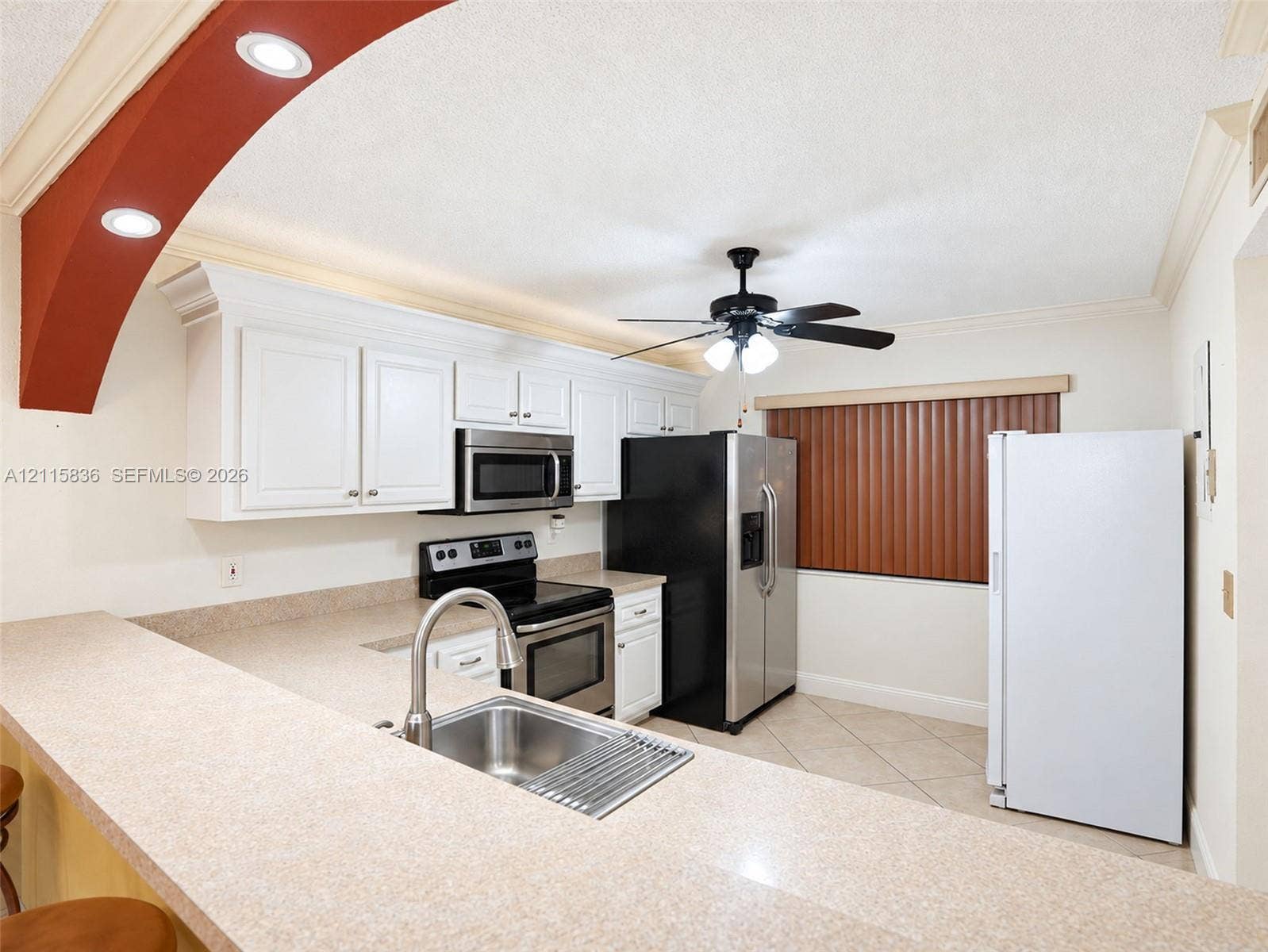 8000 Hampton Boulevard, #311, North Lauderdale, North Lauderdale, FL 33068 Kitchen featuring white cabinetry, solid-surface countertops, integrated breakfast bar with stainless steel sink, recessed lighting, and an arched architectural detail