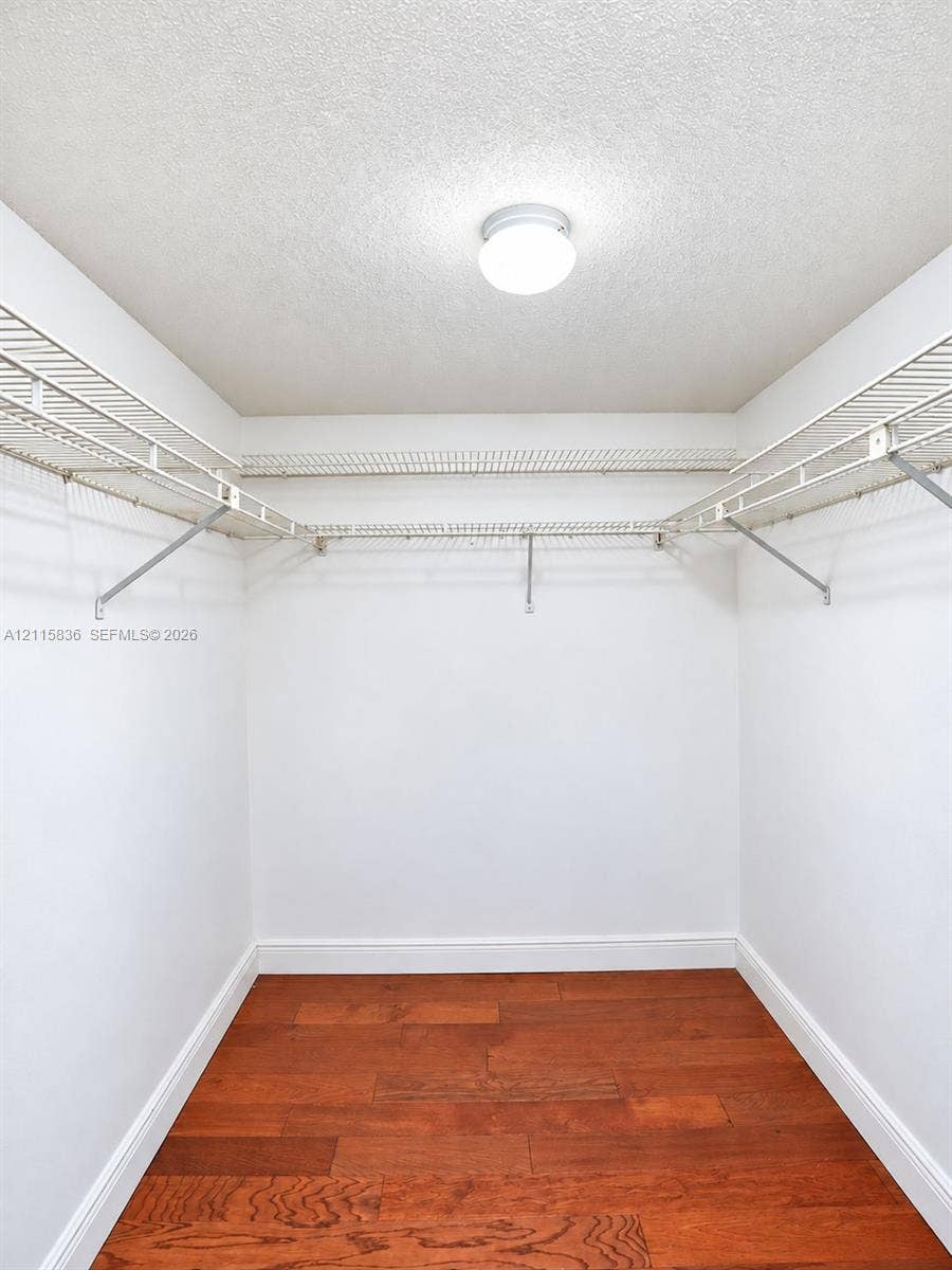 8000 Hampton Boulevard, #311, North Lauderdale, North Lauderdale, FL 33068 Walk-in closet featuring wood-finish flooring, white walls, and tiered metal wire shelving with an integrated ceiling-mounted light fixture