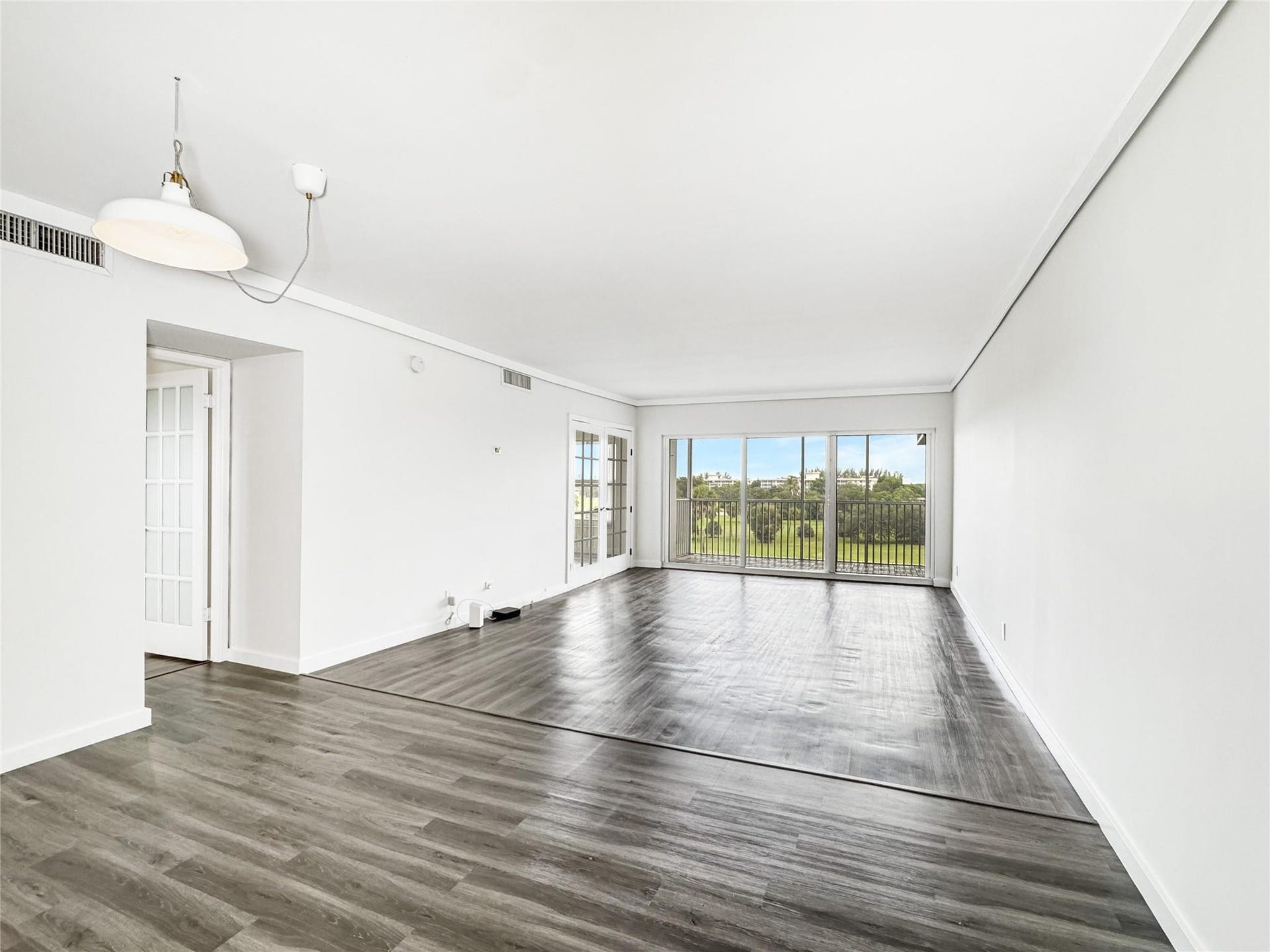 2950 N Palm Aire Drive, #506, Pompano Beach, FL 33069 Expansive living area showcases vinyl flooring, oversized sliding glass doors, and access to the screened balcony overlooking open green space. The open layout provides ample room for both seating and dining areas.