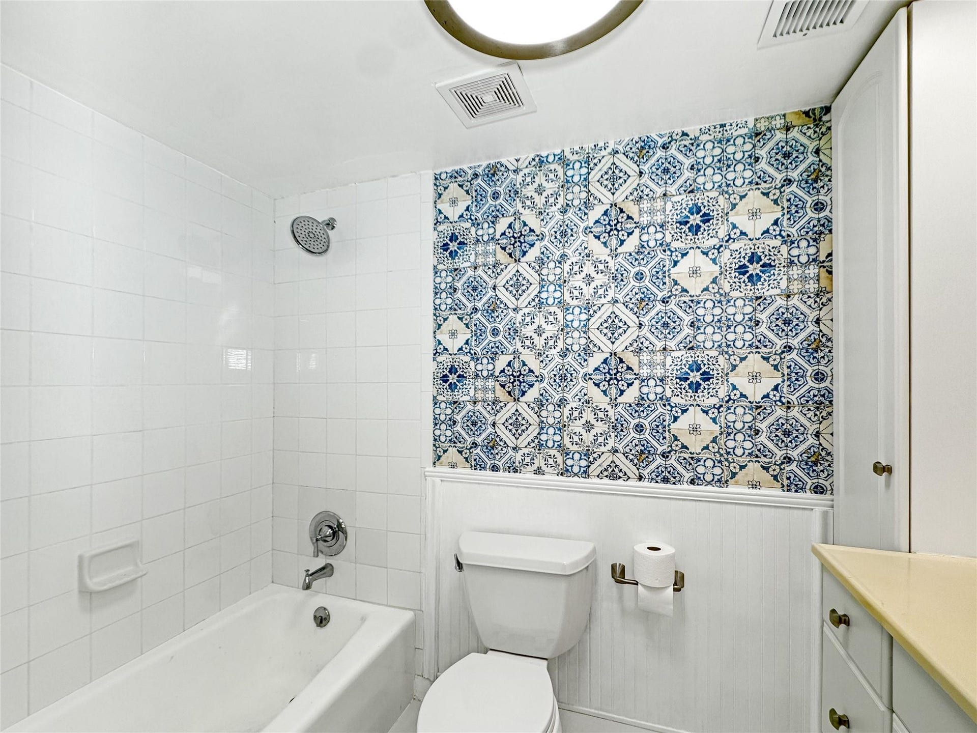 2950 N Palm Aire Drive, #506, Pompano Beach, FL 33069 Bathroom features a tub and shower combination with white tile surround and decorative blue accent walls. Vanity storage and updated lighting enhance the space.