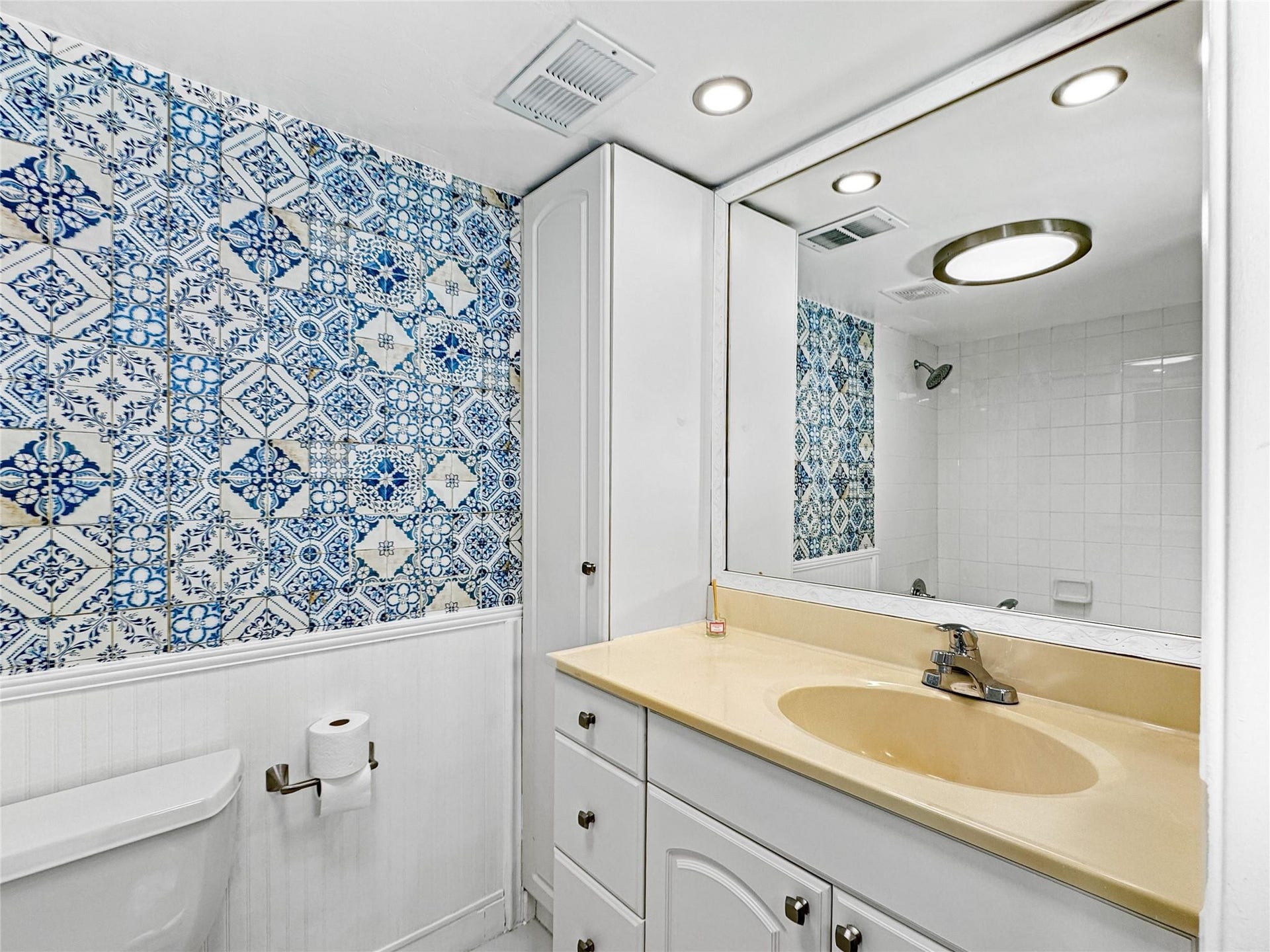 2950 N Palm Aire Drive, #506, Pompano Beach, FL 33069 Primary Bathroom includes a single-sink vanity with ample cabinet storage and decorative blue patterned accent walls. Bright lighting and neutral finishes create a fresh, functional space.
