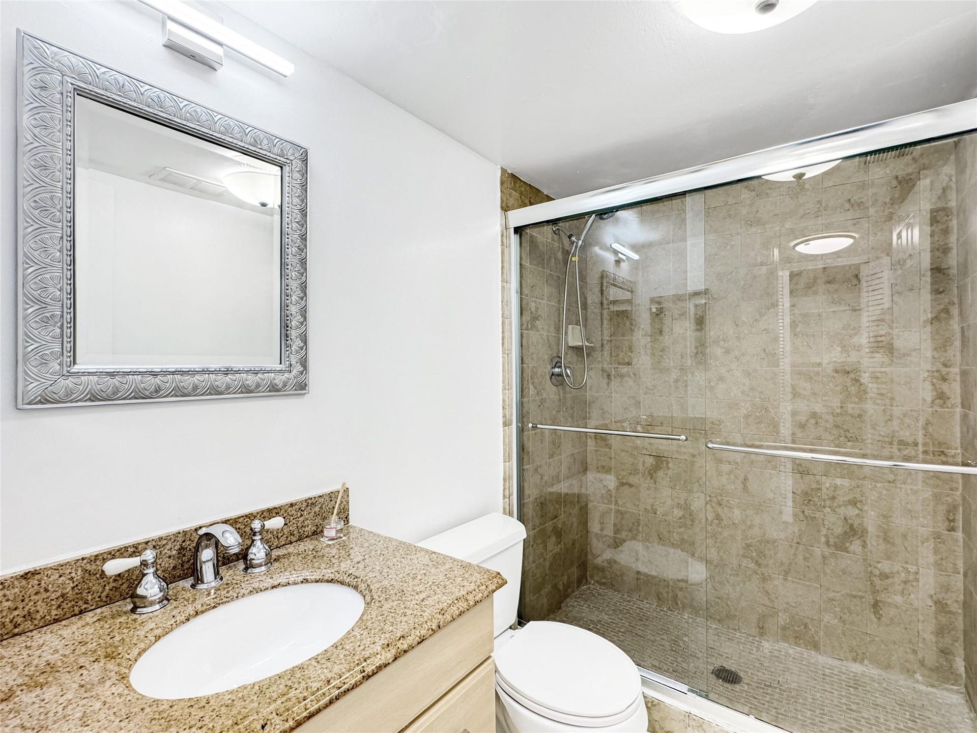 2950 N Palm Aire Drive, #506, Pompano Beach, FL 33069 Bathroom features a granite-style vanity countertop, updated fixtures, and a large glass-enclosed walk-in shower with tile surround. Neutral finishes create a clean and polished look.