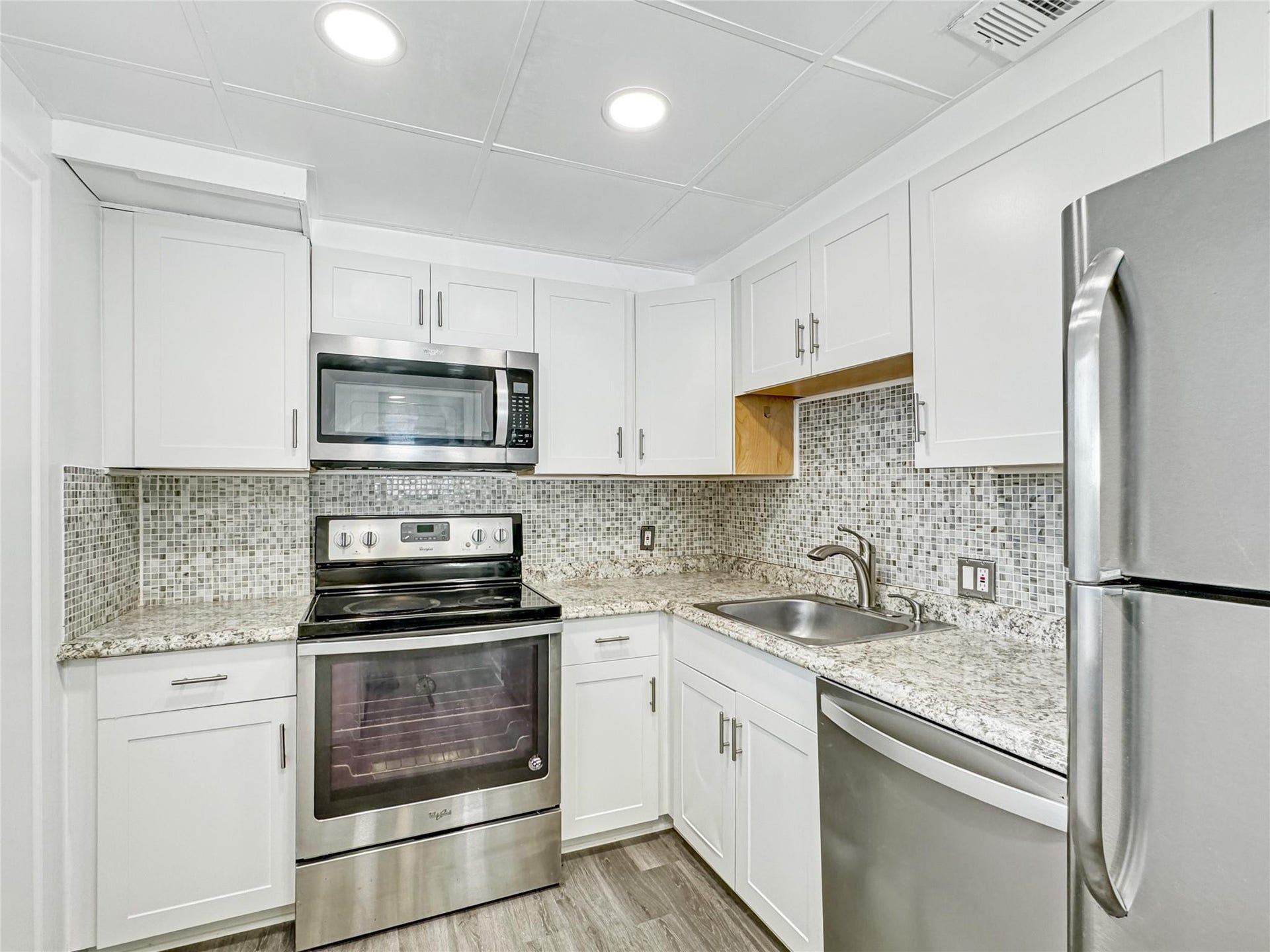 2950 N Palm Aire Drive, #506, Pompano Beach, FL 33069 Kitchen features white shaker-style cabinetry, granite-style countertops, mosaic tile backsplash, and stainless steel appliances. Recessed lighting and vinyl flooring complete the clean, updated design.