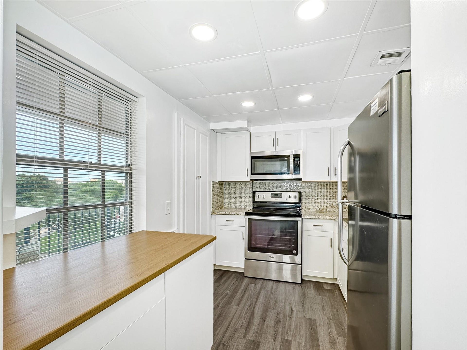 2950 N Palm Aire Drive, #506, Pompano Beach, FL 33069 Kitchen offers a functional layout with stainless steel appliances, granite-style countertops, and white cabinetry. A mobile prep island with additional storage adds flexibility and convenience to the space.