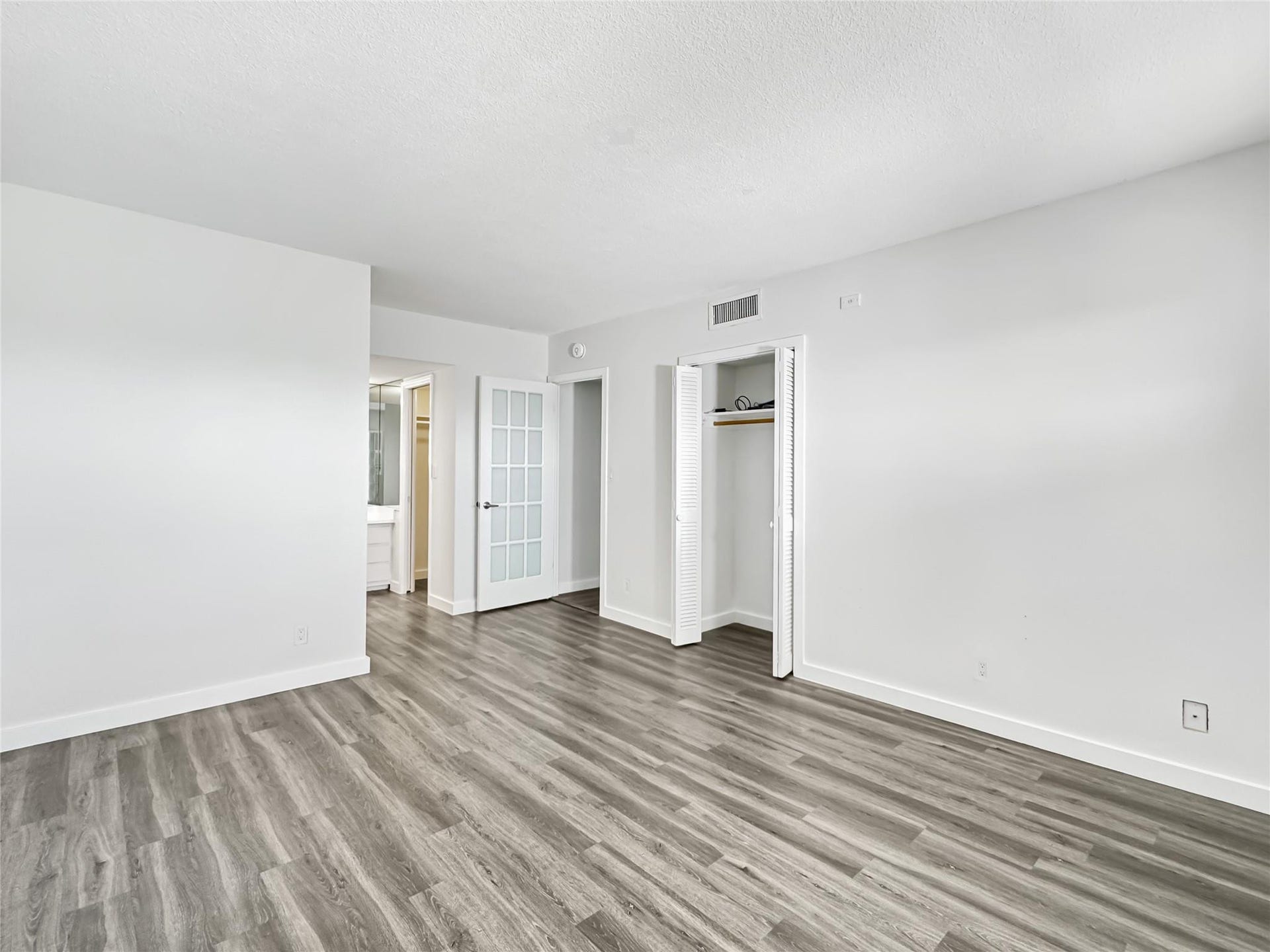 2950 N Palm Aire Drive, #506, Pompano Beach, FL 33069 Bedroom offers an open layout with adjoining vanity and dressing area access. Vinyl flooring and soft neutral tones create a bright and inviting atmosphere.