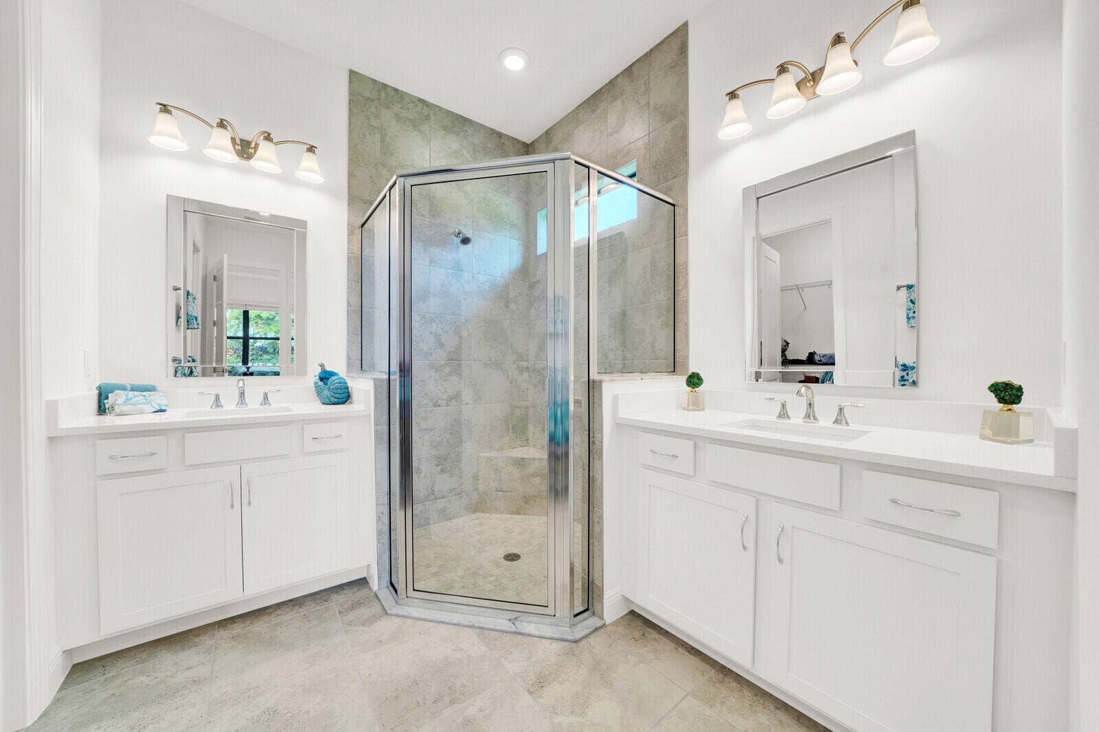Spacious bathroom featuring a glass-enclosed shower with tile surround, dual vanity sinks, white cabinetry, polished chrome fixtures, and large format tile flooring